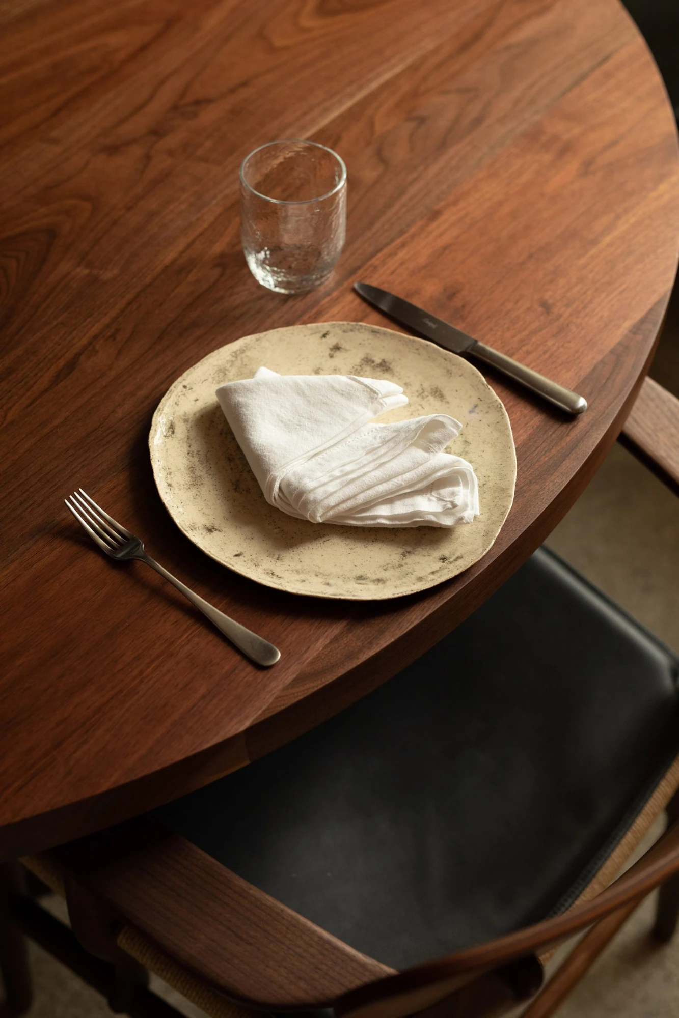Cozinha das Flores Mural by Álvaro Siza, photographed by Luís Moreira — Place setting at Cozinha das Flores: a speckled ceramic plate, folded linen napkin and worn silver on dark wood.
