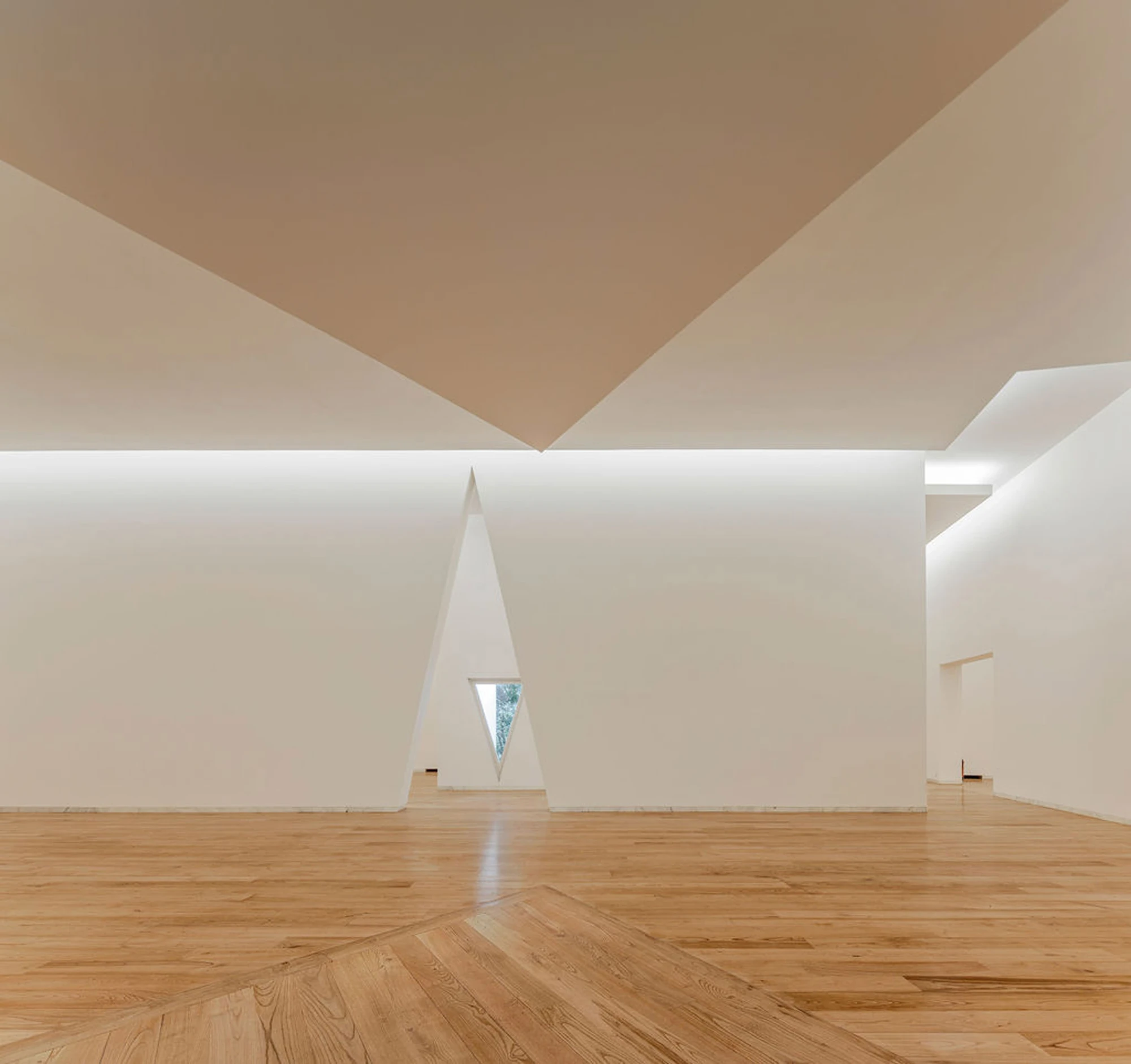 Serralves Museum New Wing by Álvaro Siza — Empty gallery in the Álvaro Siza Wing with pale wood floorboards, a folded ceiling and a tall triangular opening cut to a sliver of green.