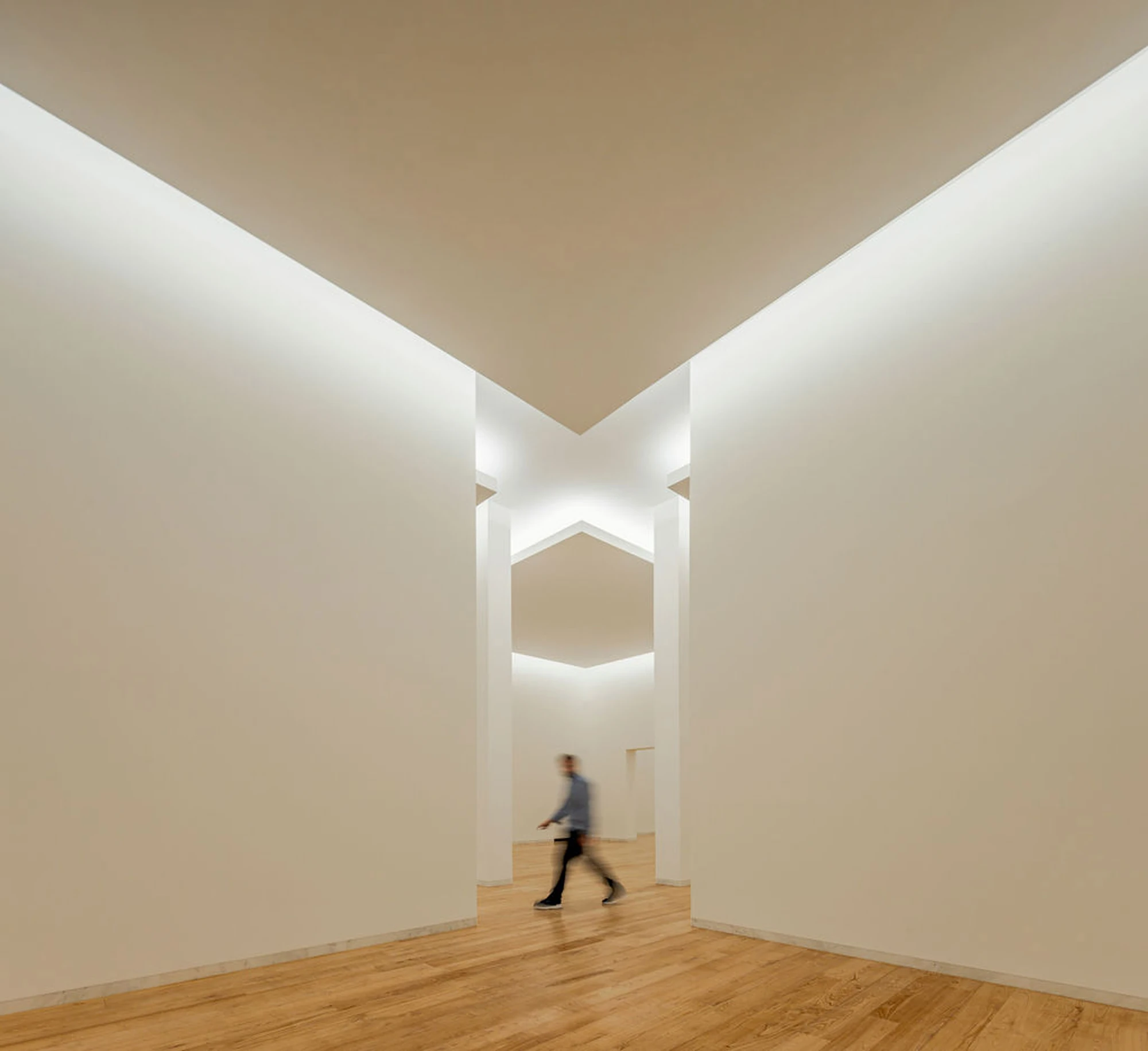 Serralves Museum New Wing by Álvaro Siza — A visitor crossing between white gallery walls in the Álvaro Siza Wing, under a folded ceiling washed by a continuous slot of light.