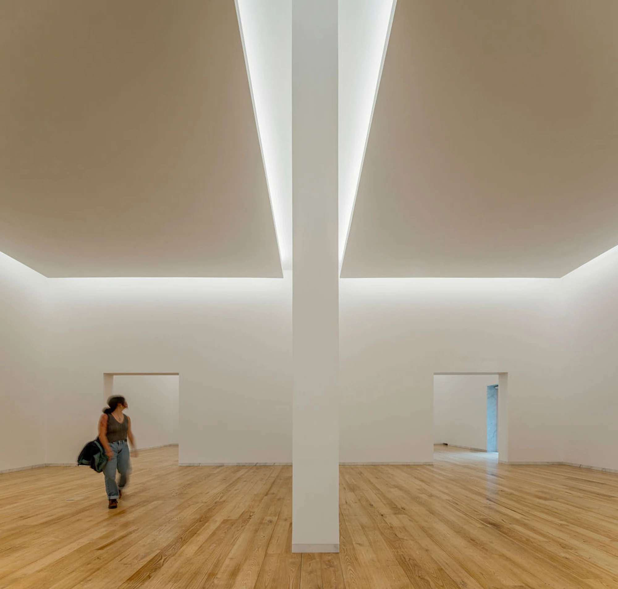 Serralves Museum New Wing by Álvaro Siza — Gallery in the Álvaro Siza Wing split by a white pier, light running the length of the ceiling above pale wood boards.