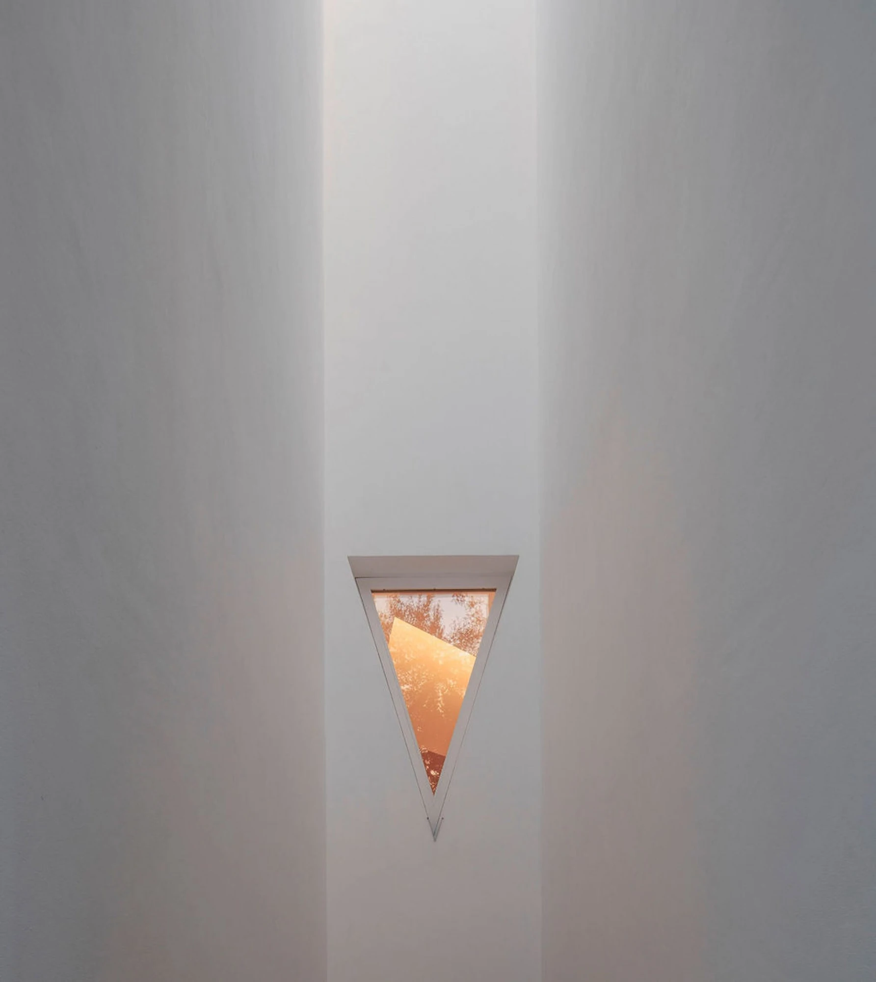 Serralves Museum New Wing by Álvaro Siza — An inverted triangular window set into a white wall of the Álvaro Siza Wing, holding a fragment of tree and evening sky.