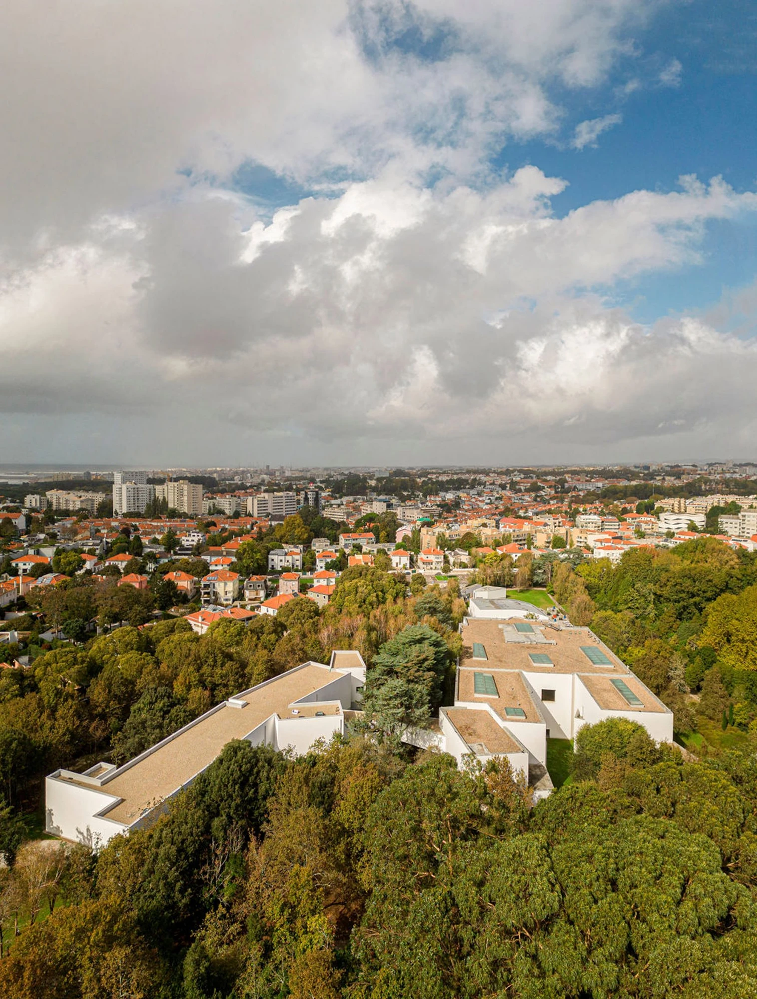 Serralves Museum New Wing by Álvaro Siza — The white roofs of the Serralves Museum spread through the park canopy, with the red tiled rooftops of Porto beyond.