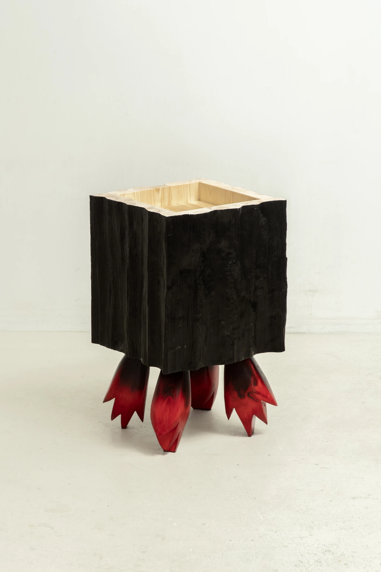 In Between Wood and Fire by Didi NG Wing Yin, photographed by Didi NG Wing Yin — Rocket Side Table No.2 standing on four red legs cut to points, its carbonised box open at the top to a pale lining.
