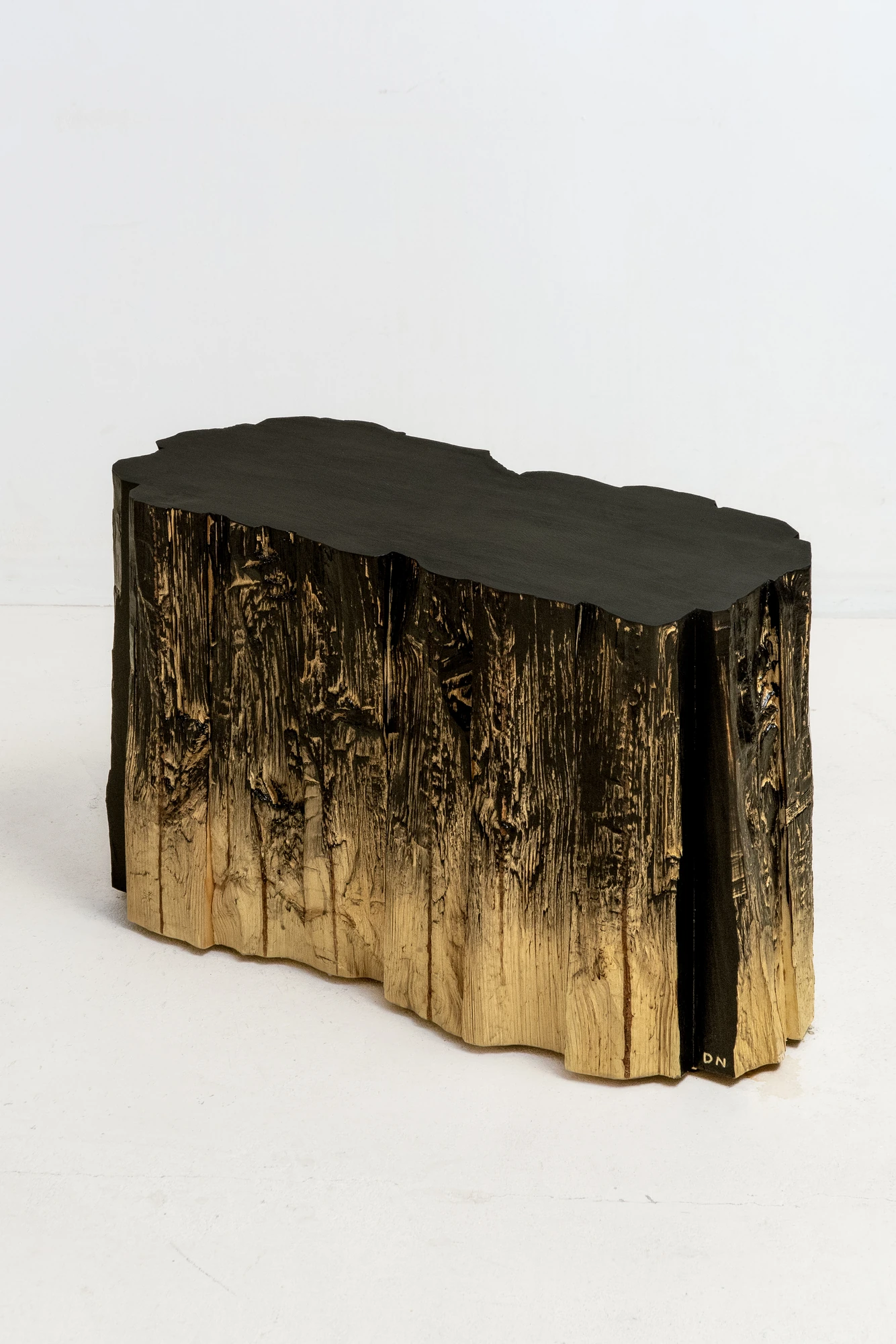 In Between Wood and Fire by Didi NG Wing Yin, photographed by Didi NG Wing Yin — Pith Stool B in three-quarter view, a long low body of split and torn faces under a flat matte black seat.