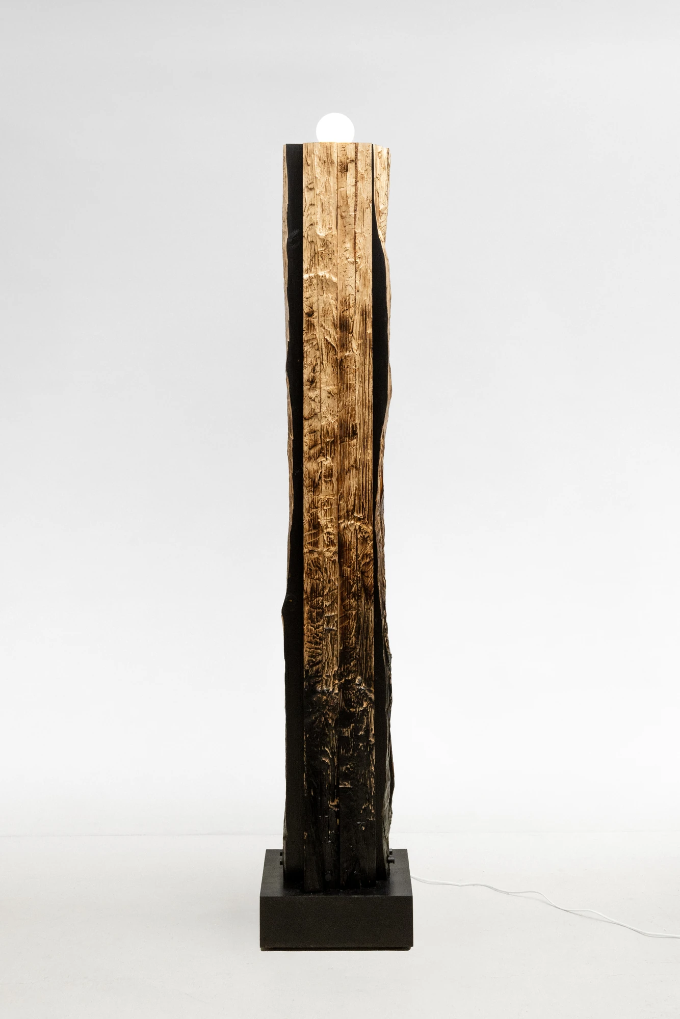 In Between Wood and Fire by Didi NG Wing Yin, photographed by Didi NG Wing Yin — The Pith Floor Lamp in full, a split length of lumber standing on a dark base with an opal globe at its top and the char heaviest at the foot.