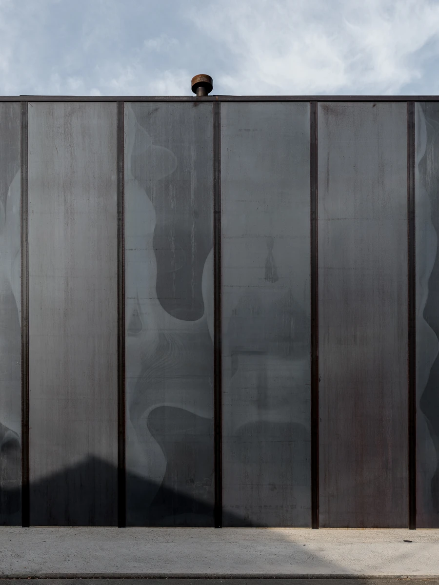 Shironishi Office by Tomoaki Uno Architects, photographed by Nathanael Bennett — The long elevation seen flat on, hot-rolled plate divided into bays by exposed steel flanges, mill scale clouding across the panels.