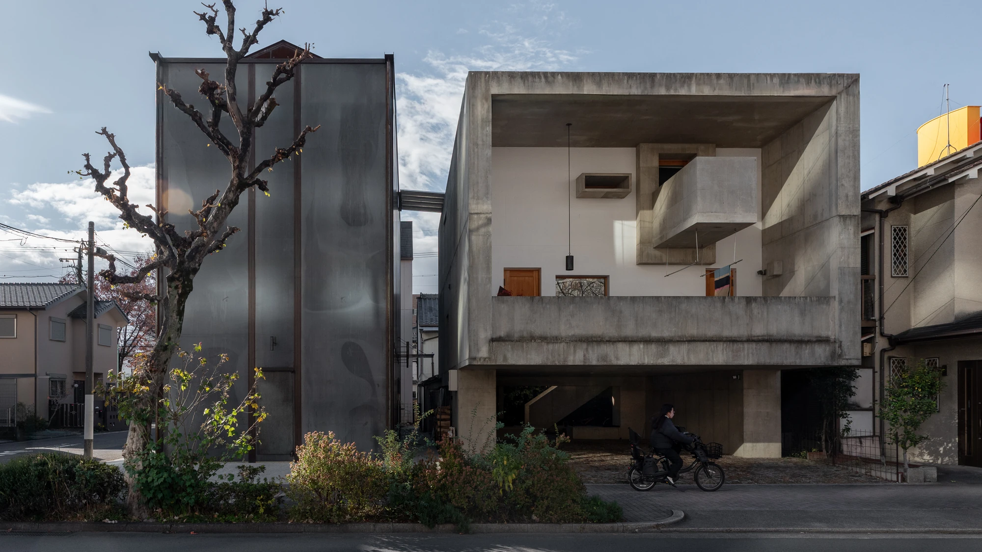 Shironishi Office by Tomoaki Uno Architects, photographed by Nathanael Bennett — The steel volume stands beside the concrete house on the neighbouring plot, a cyclist passing between the two.