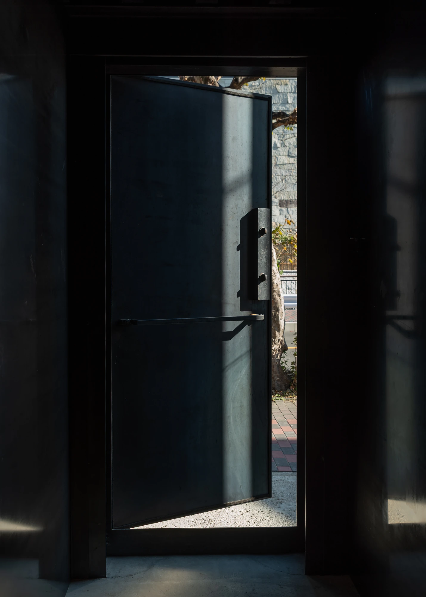 Shironishi Office by Tomoaki Uno Architects, photographed by Nathanael Bennett — The door pushed ajar from inside, daylight running down the plate and out to a stone wall and the trunk of a tree.