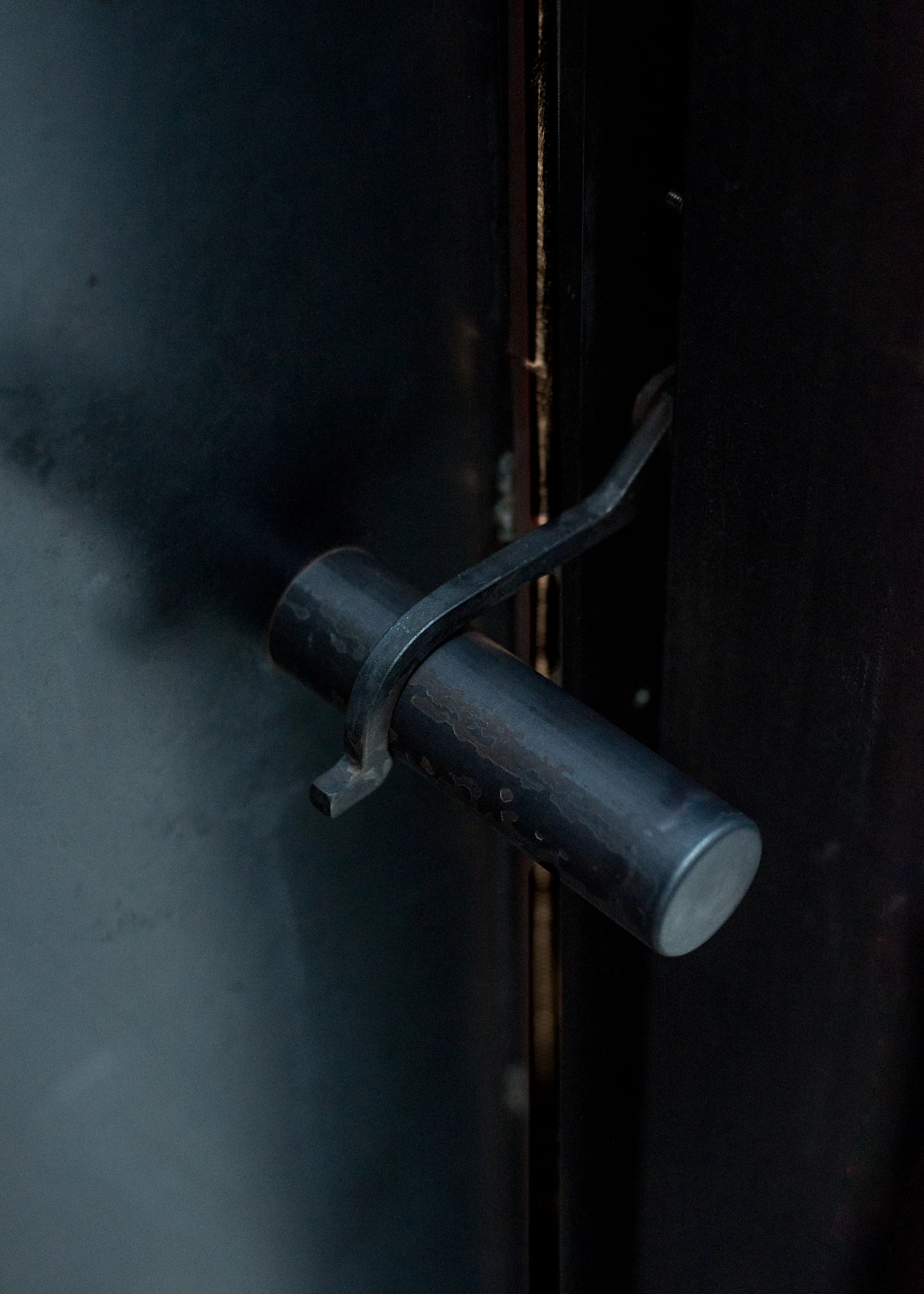 Shironishi Office by Tomoaki Uno Architects, photographed by Nathanael Bennett — Close on the lever, a solid steel cylinder crossed by a hand-formed latch, against near-black plate.