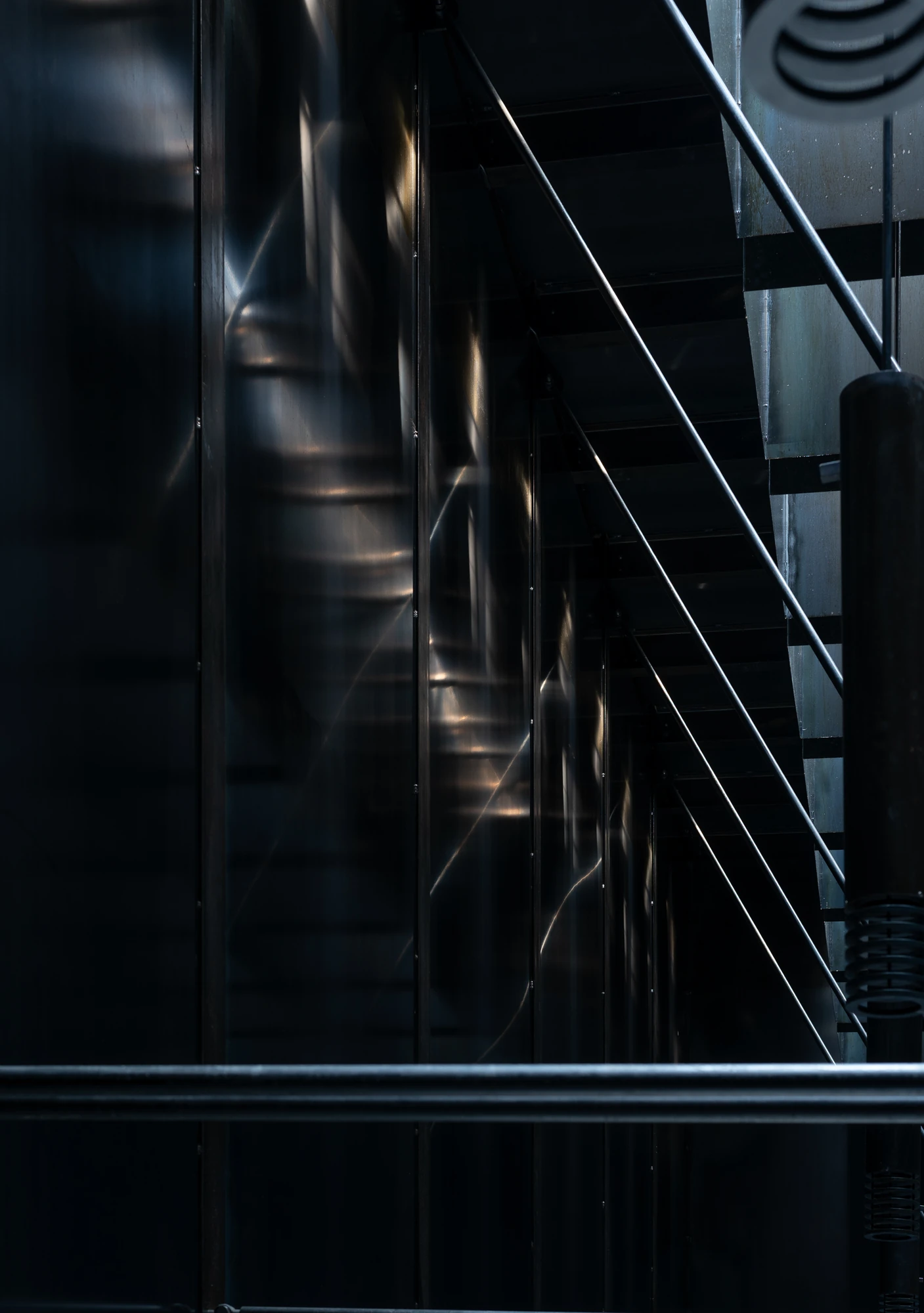 Shironishi Office by Tomoaki Uno Architects, photographed by Nathanael Bennett — Light sliding across the plate wall beside the stair, the sheen of the rolled surface caught along the seams.