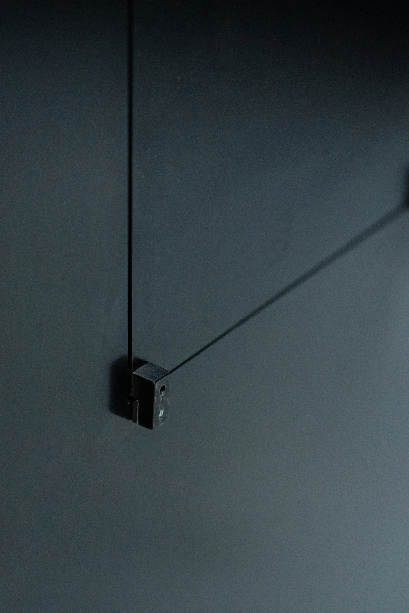 Shironishi Office by Tomoaki Uno Architects, photographed by Nathanael Bennett — A small welded bracket holding a thin rod against a dark panel, its shadow thrown out to one side.