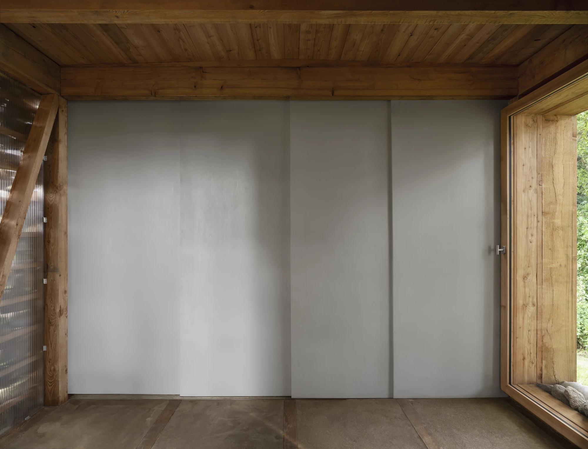HAIN by undjurekbrüggen, photographed by Hannes Heitmüller — A wall of grey sliding panels beneath an exposed larch beam and boarded ceiling, closing off the service zone.