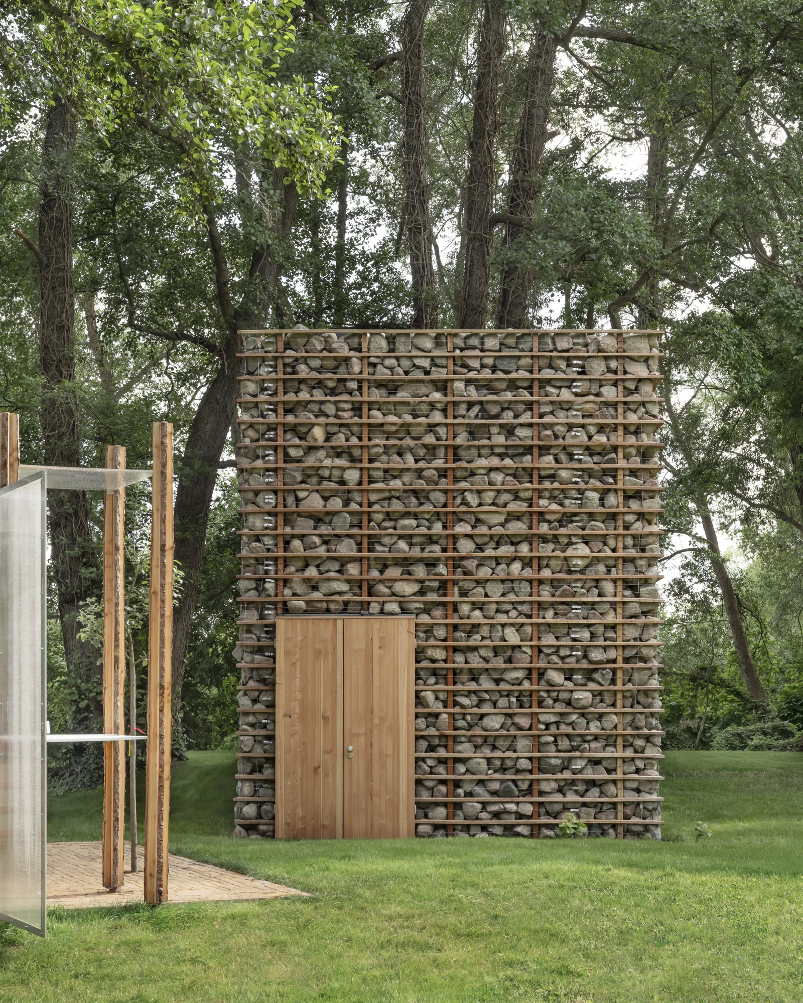 HAIN by undjurekbrüggen, photographed by Hannes Heitmüller — The fieldstone wall rising above a pair of larch doors, with the corrugated pavilion entering the frame at the left.