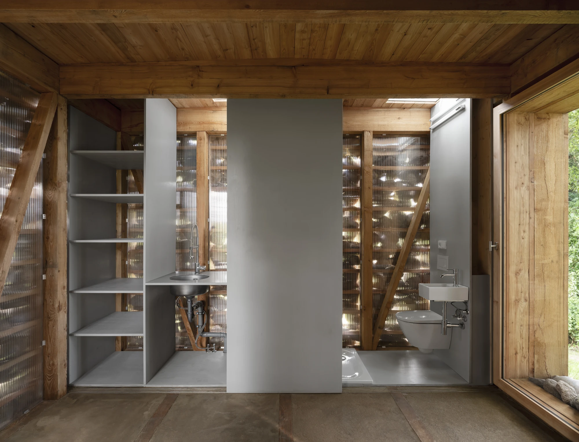 HAIN by undjurekbrüggen, photographed by Hannes Heitmüller — The service panels slid open to reveal a stainless sink, grey shelving and a washroom set against the corrugated skin.