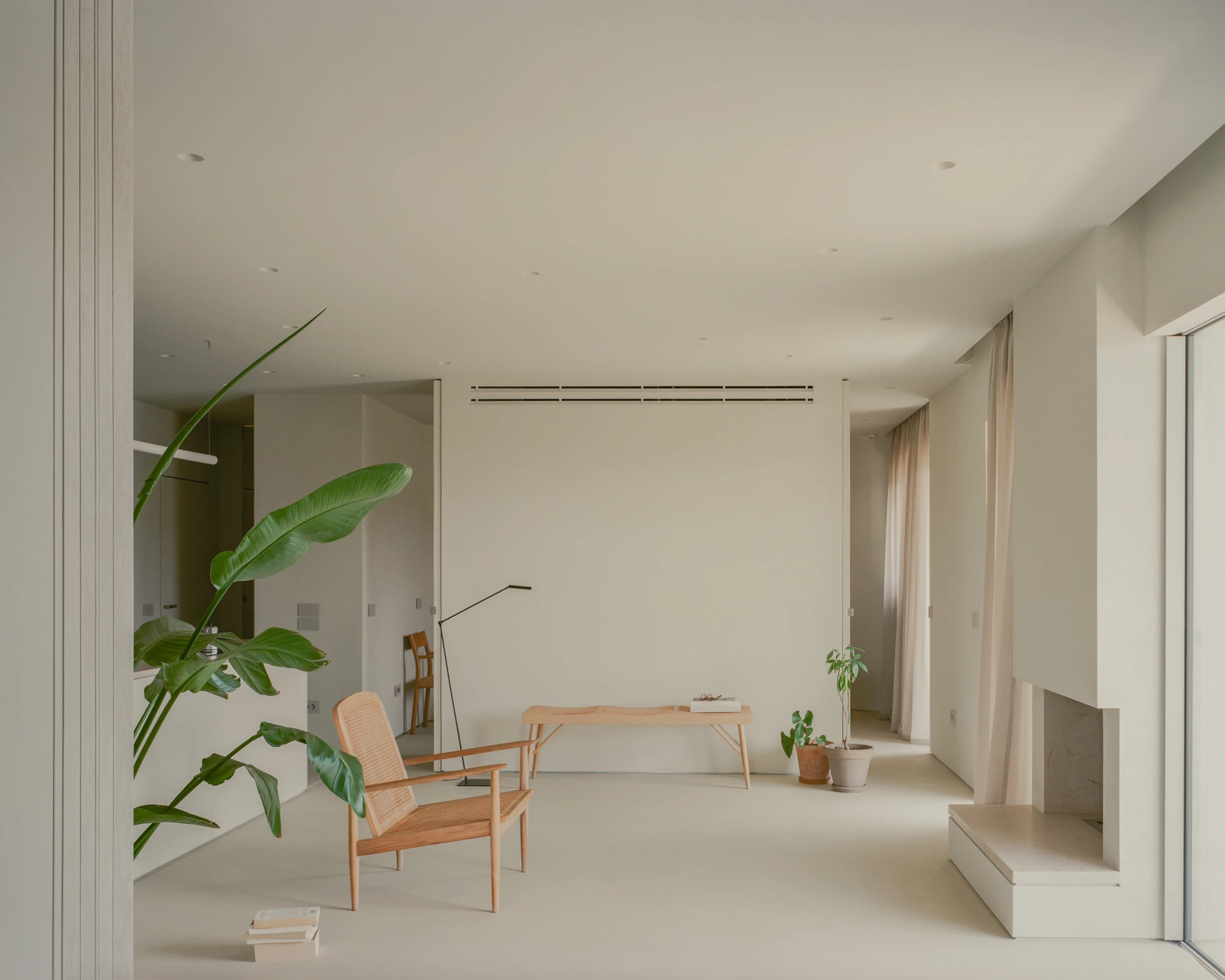 Kifisia Apartment by Georgios Apostolopoulos Architects, photographed by Lorenzo Zandri — The living area with a caned lounge chair, a low oak bench and a stone-faced window seat built into the right-hand wall.