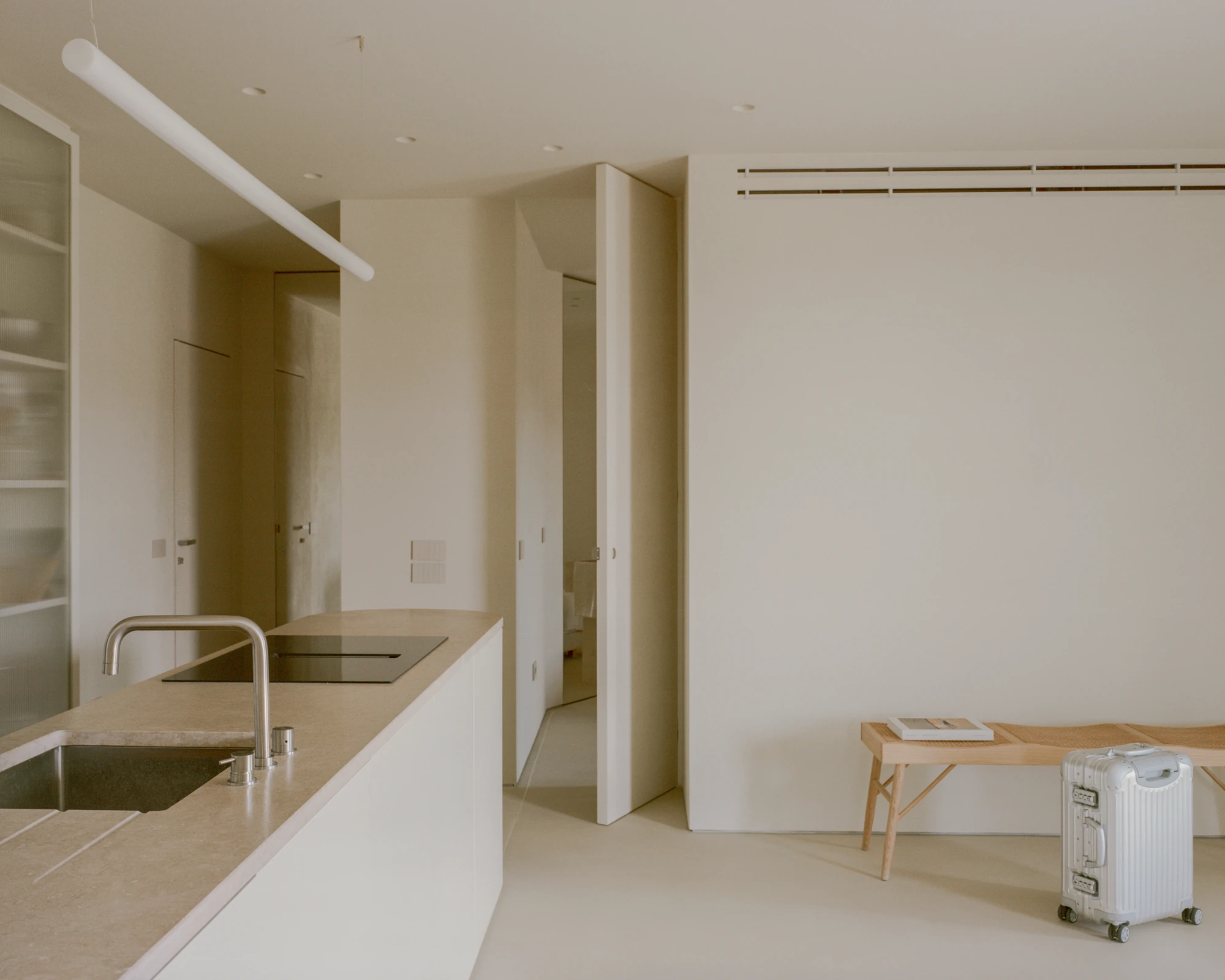 Kifisia Apartment by Georgios Apostolopoulos Architects, photographed by Lorenzo Zandri — The stone counter with sink and hob in the foreground, a run of flush doors and a caned bench in the distance.