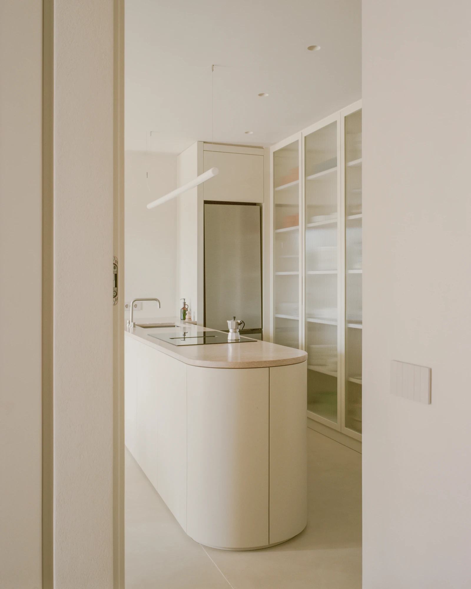 Kifisia Apartment by Georgios Apostolopoulos Architects, photographed by Lorenzo Zandri — The kitchen island seen through a doorway, its curved end turning toward floor-to-ceiling reeded glass storage.