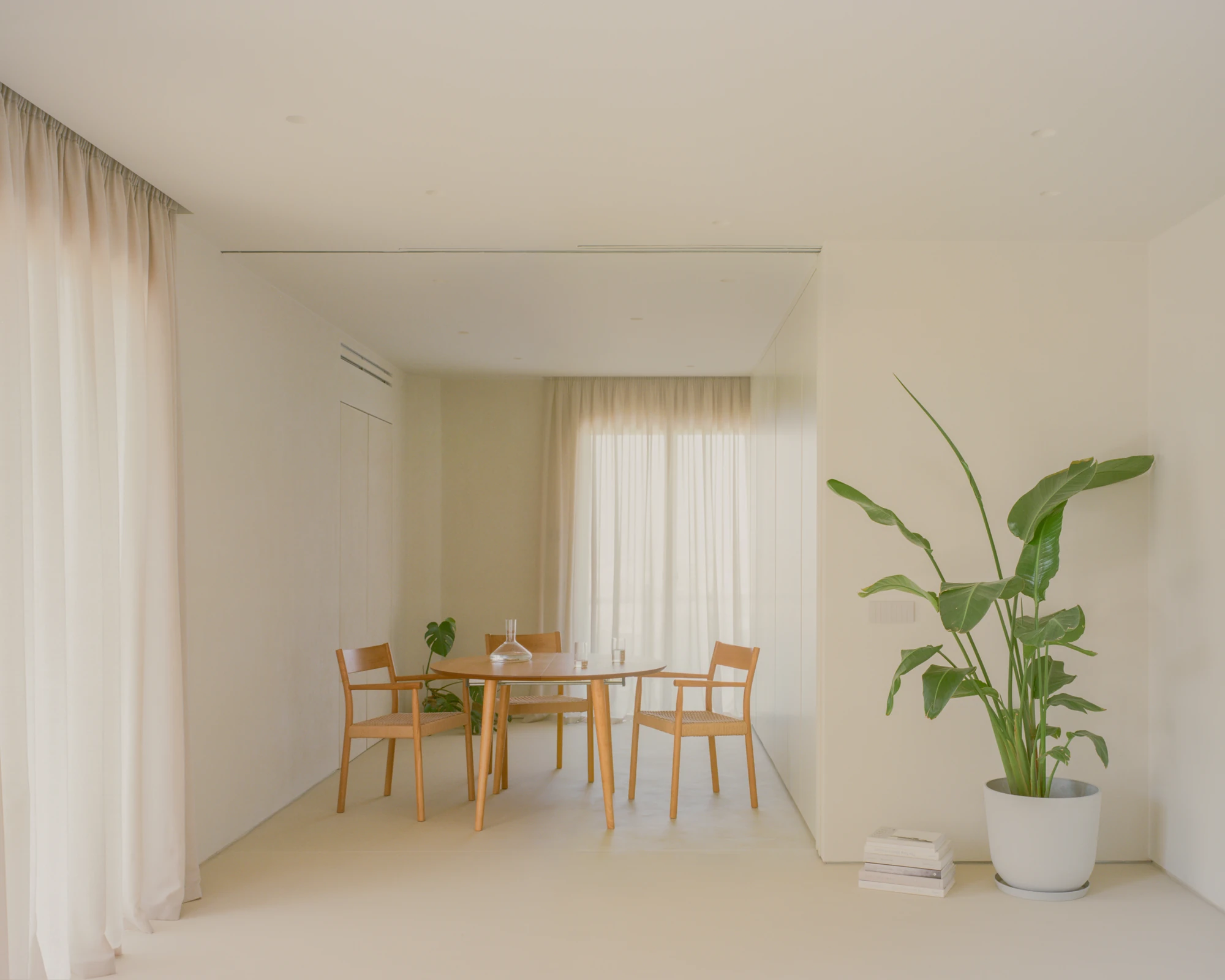 Kifisia Apartment by Georgios Apostolopoulos Architects, photographed by Lorenzo Zandri — The dining area with a round oak table and three caned armchairs set against a sheer-curtained window.