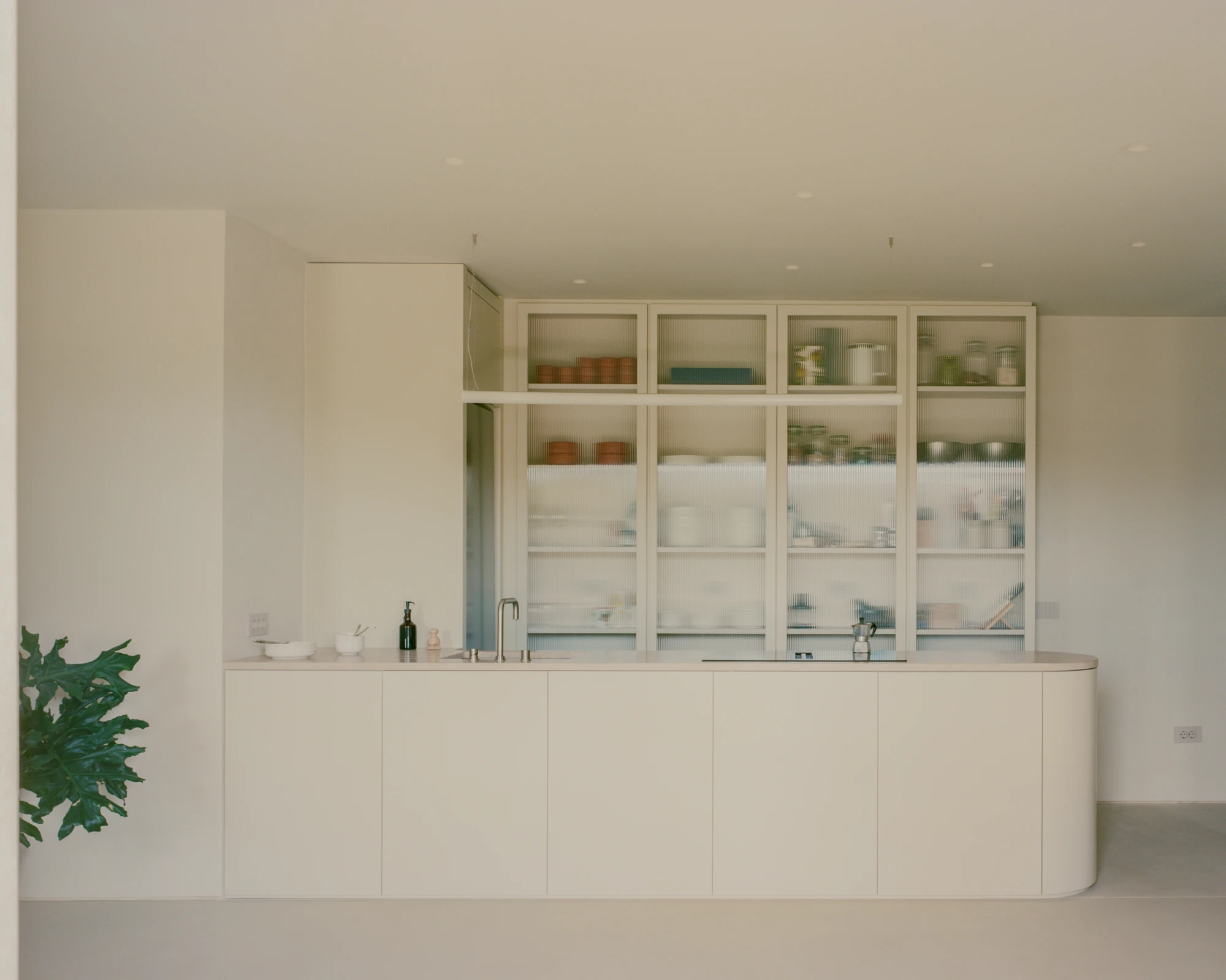 Kifisia Apartment by Georgios Apostolopoulos Architects, photographed by Lorenzo Zandri — The kitchen elevation head on, reeded glass cabinetry stacked above a continuous pale counter and a rounded cabinet end.
