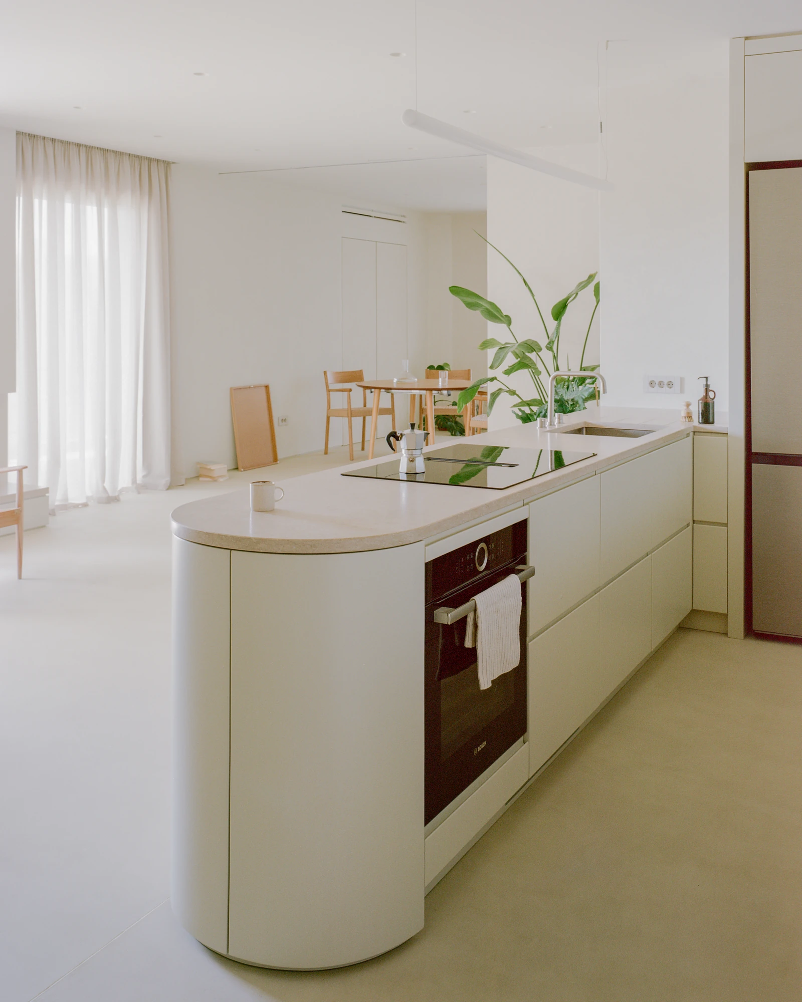 Kifisia Apartment by Georgios Apostolopoulos Architects, photographed by Lorenzo Zandri — The kitchen volume in profile, a rounded end and pale stone counter carrying an induction hob and sink, the dining area beyond.