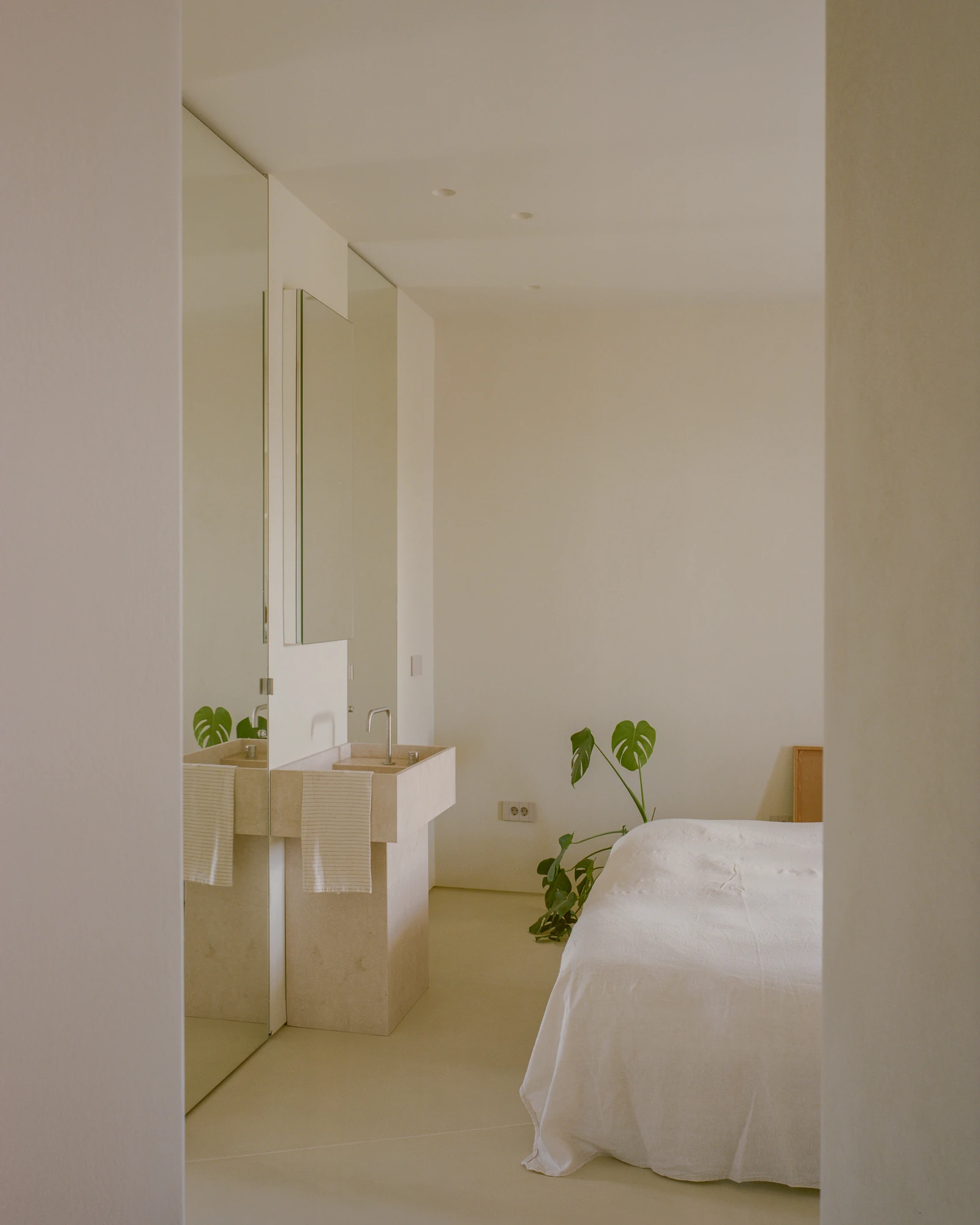 Kifisia Apartment by Georgios Apostolopoulos Architects, photographed by Lorenzo Zandri — The vanity block seen from the bed, a slim mirror above it and full-height mirrored wardrobe fronts reflecting the curtained window.