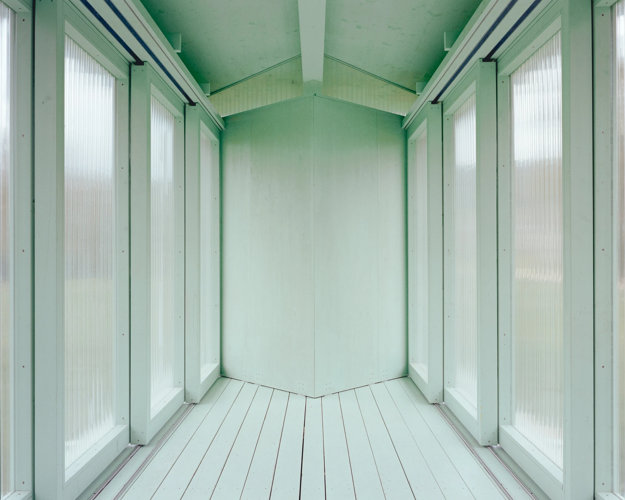 Pavilion of the Sliding Doors by Piertzovanis Toews, photographed by Federico Farinatti — The interior end wall in pale green boards, flanked by fluted polycarbonate panels on both sides and lit evenly through them.