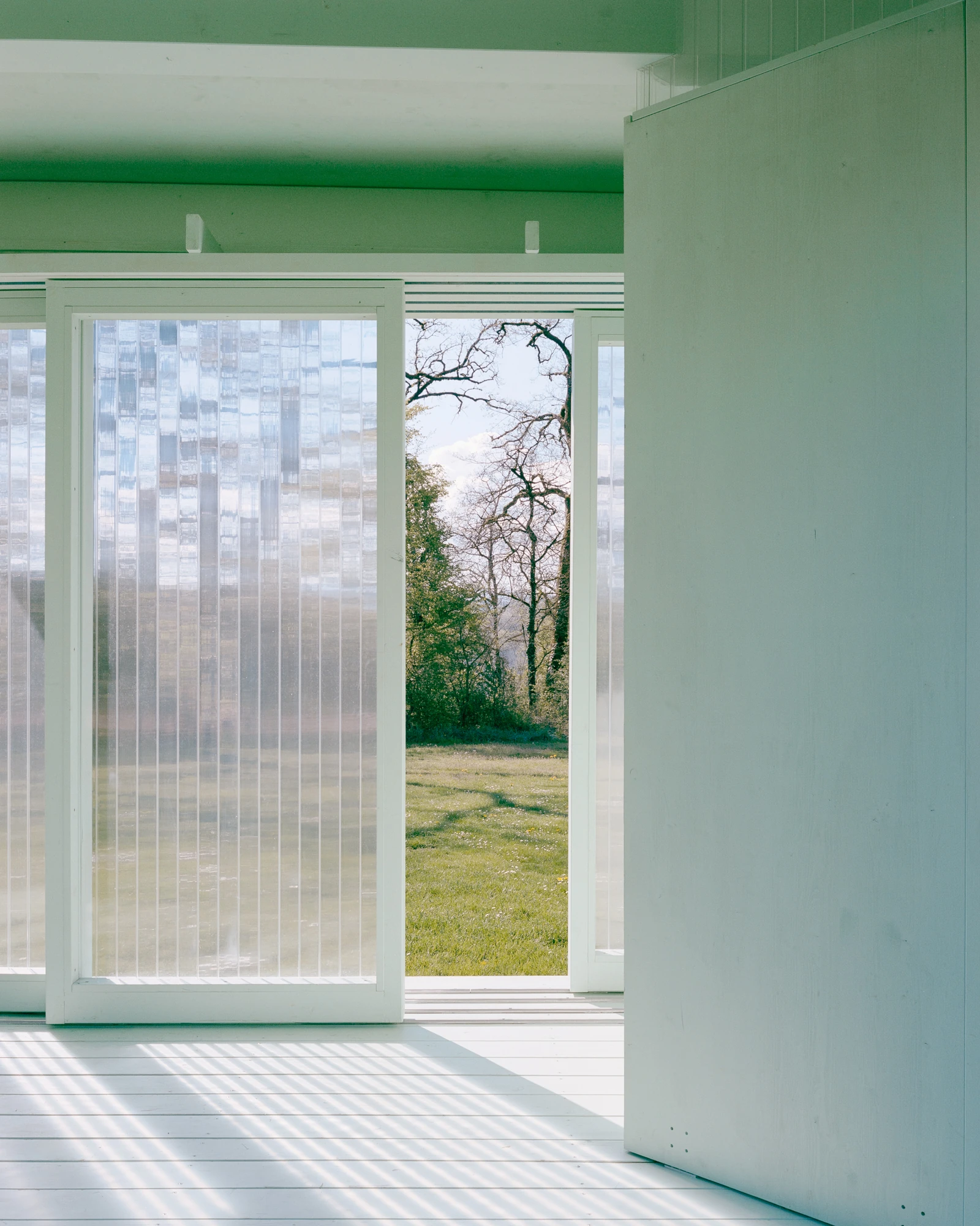 Pavilion of the Sliding Doors by Piertzovanis Toews, photographed by Federico Farinatti — Interior view with one sliding panel pushed open onto the meadow and a bare tree.