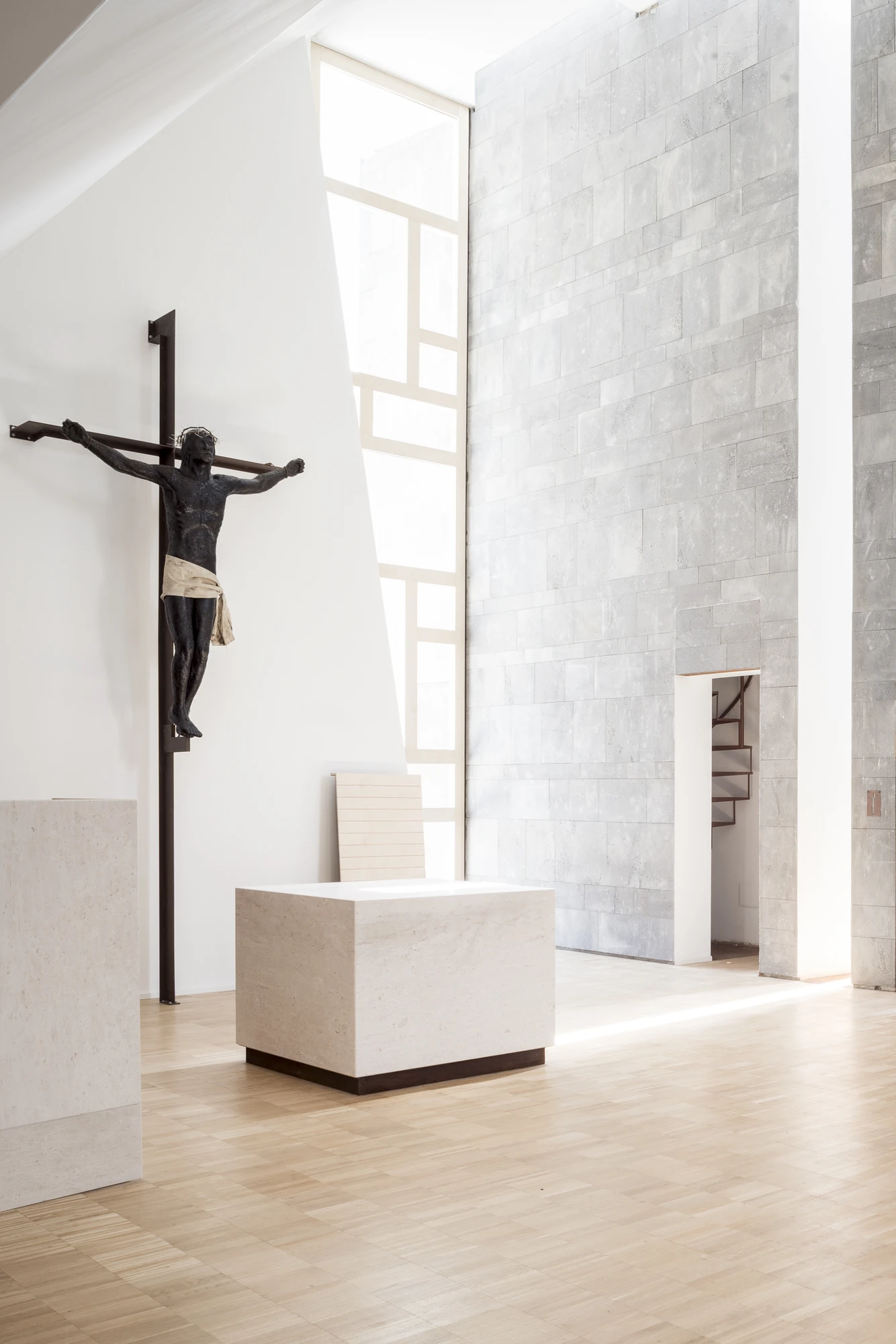 Complesso parrocchiale e Chiesa della Beata Vergine Assunta by Carlo Atzeni, Silvia Mocci, Maurizio Manias, Franceschino Serra, photographed by Studio Vetroblu — The black crucifix hangs on a slender cross against the white wall, facing the marble altar…
