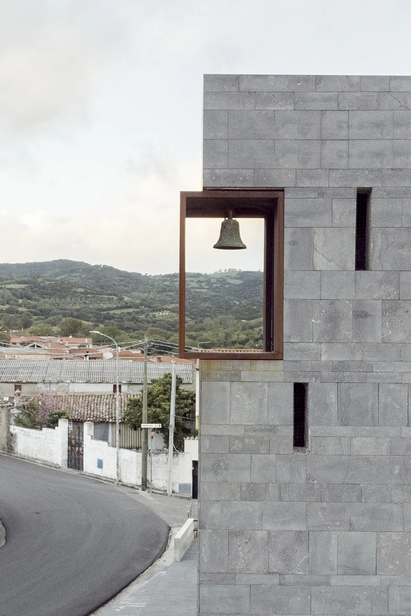 Complesso parrocchiale e Chiesa della Beata Vergine Assunta by Carlo Atzeni, Silvia Mocci, Maurizio Manias, Franceschino Serra, photographed by Studio Vetroblu — The bell hangs in a corten lined opening cut through the basalt tower, level with the roofs…
