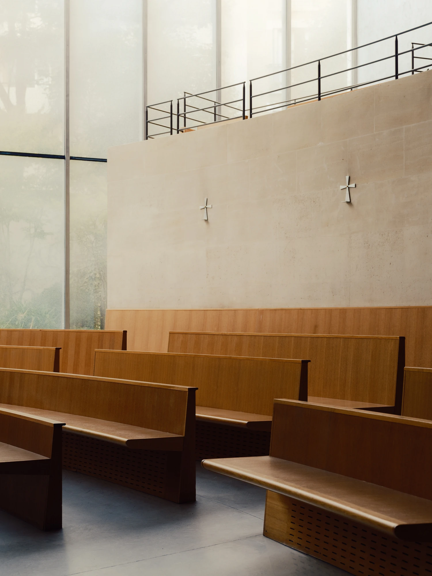 Église Saint-François de Molitor by Corinne Callies and Jean-Marie Duthilleul — A detail of empty timber benches with perforated panels along their bases, set against a pale stone wall carrying two small metal crosses.