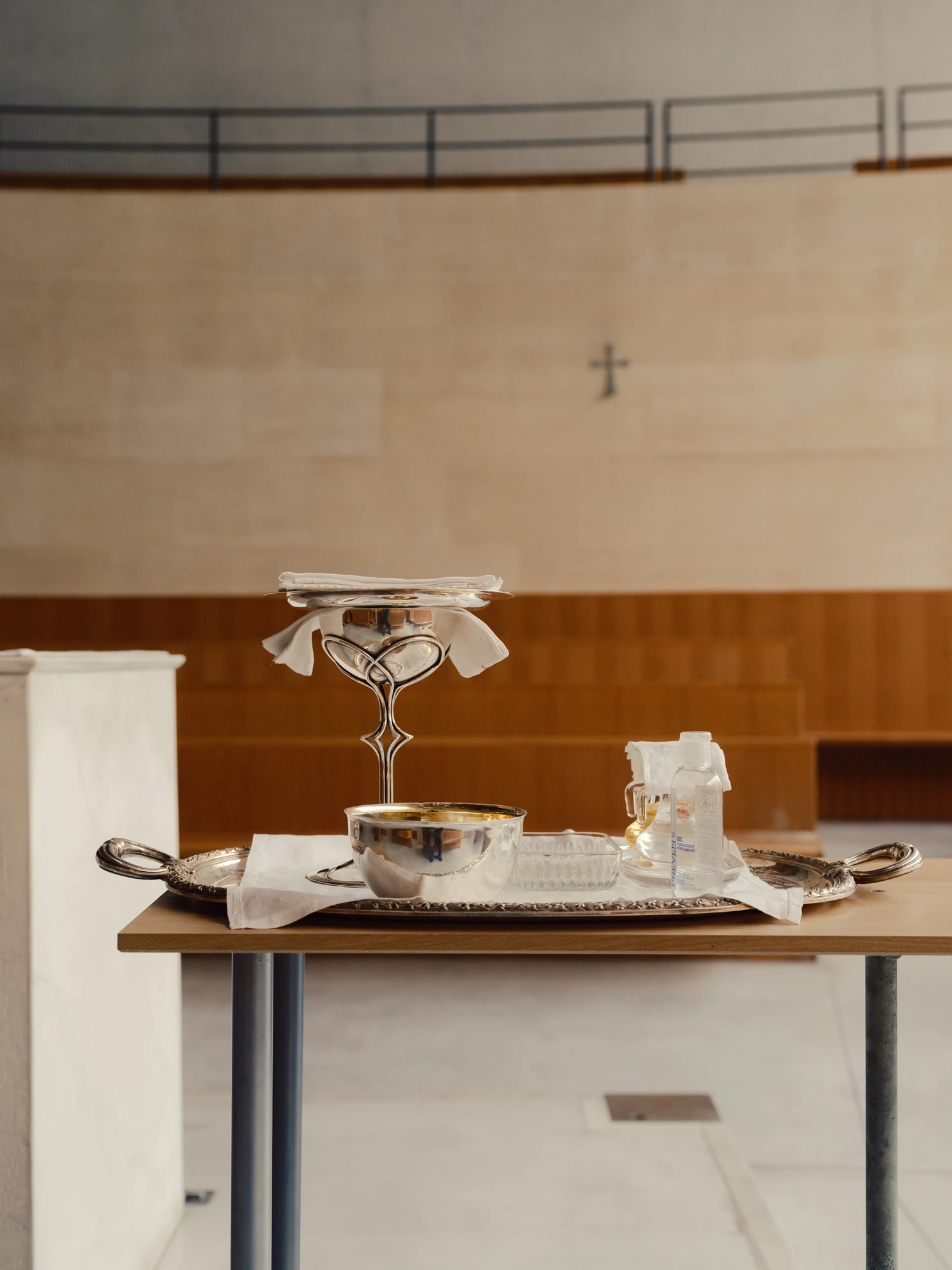 Église Saint-François de Molitor by Corinne Callies and Jean-Marie Duthilleul — A silver tray on a slim timber table holds a chalice, a bowl, a glass cruet and folded white linen.