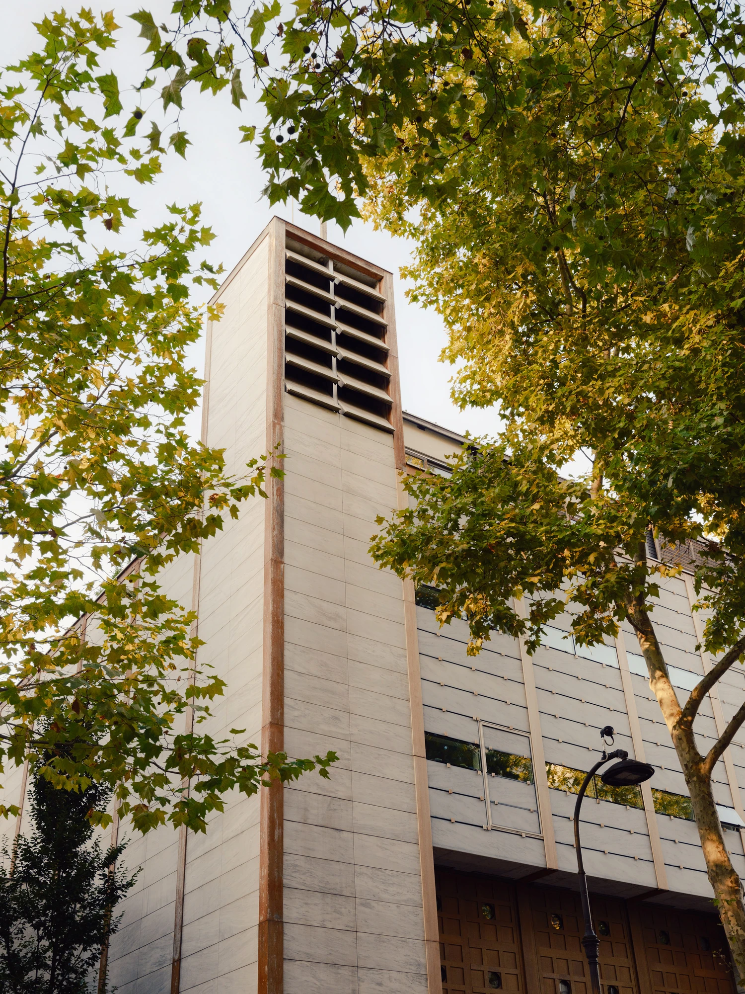 Église Saint-François de Molitor by Corinne Callies and Jean-Marie Duthilleul — The campanile seen from the pavement through plane tree leaves, its louvred bell opening set high in a shaft of marble panels.