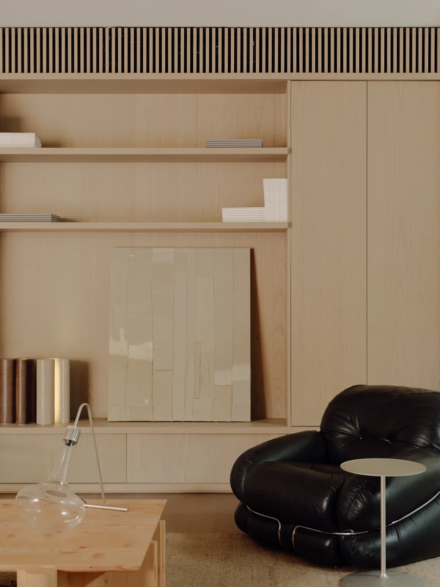 49 Walsh Street by MORQ, photographed by Tom Ross — A pale timber joinery wall with open shelves, a collaged paper panel leaning at its base and a slatted timber grille running along the top.