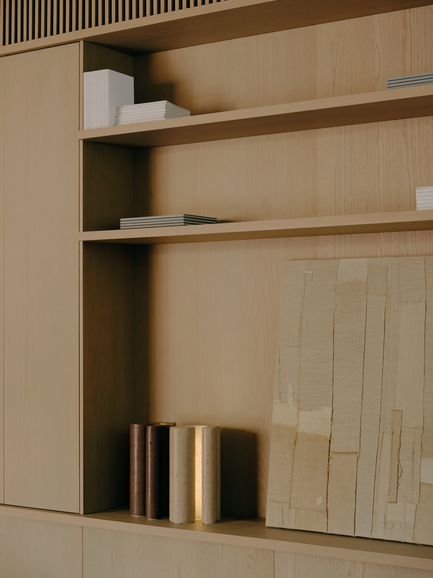 49 Walsh Street by MORQ, photographed by Tom Ross — Close view of pale timber shelving holding stacked books and a row of cylindrical bronze and travertine vessels.