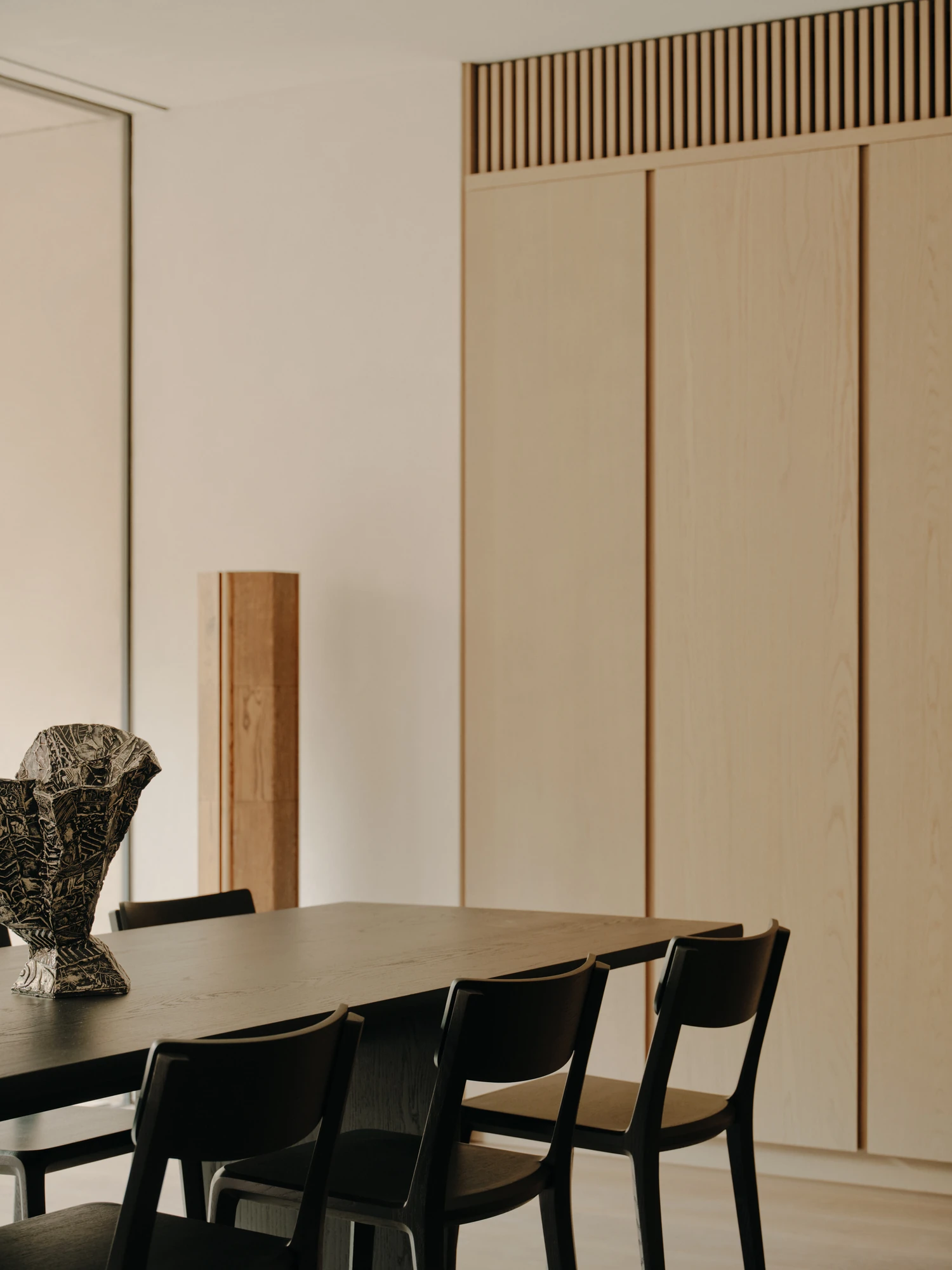 49 Walsh Street by MORQ, photographed by Tom Ross — Black timber chairs drawn up to a dark dining table, set against a run of full-height pale timber cabinetry topped by a slatted band.