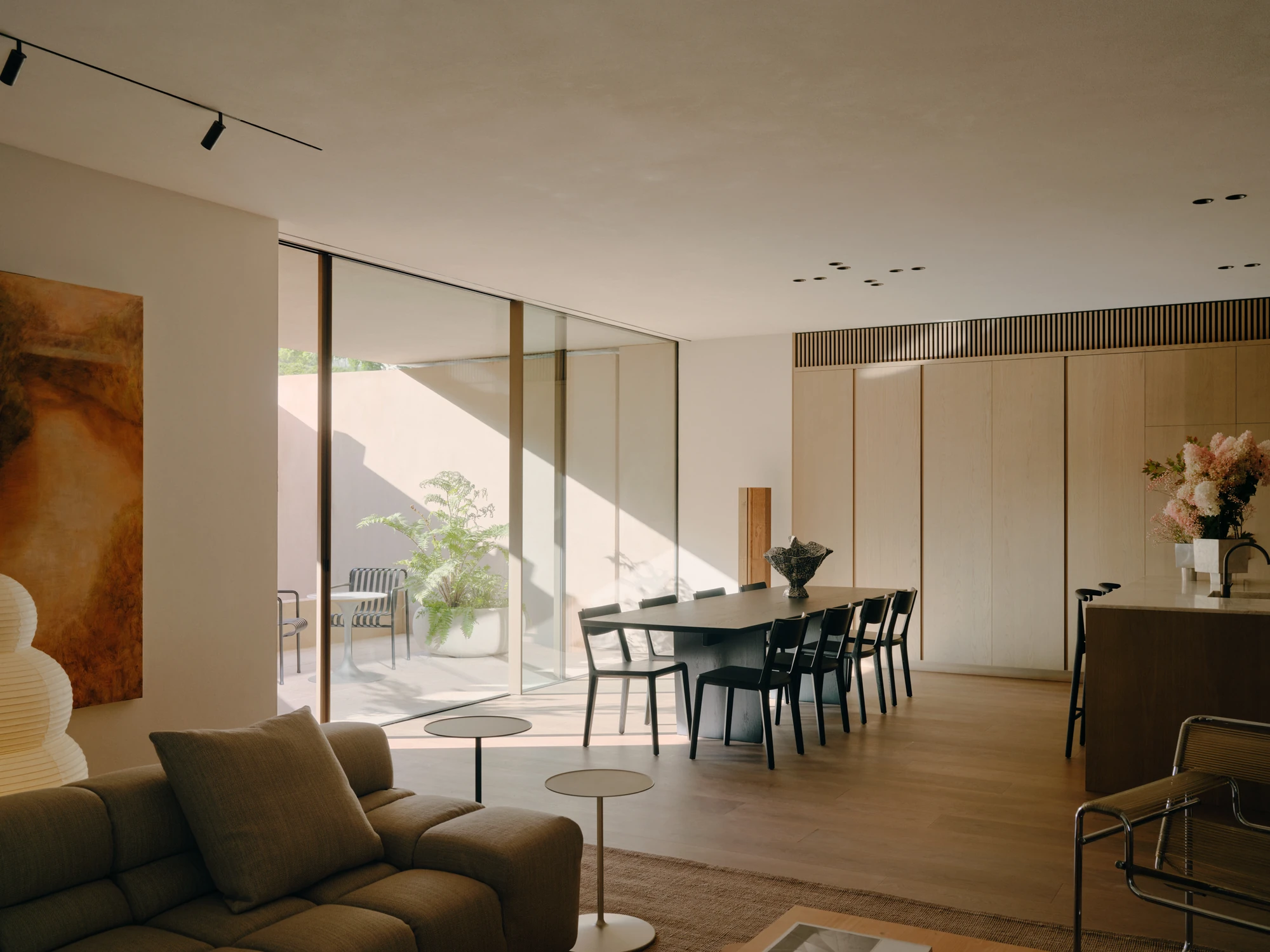 49 Walsh Street by MORQ, photographed by Tom Ross — An open-plan living and dining room with track lighting, a dark table ringed by black chairs and pale timber cabinetry beyond.