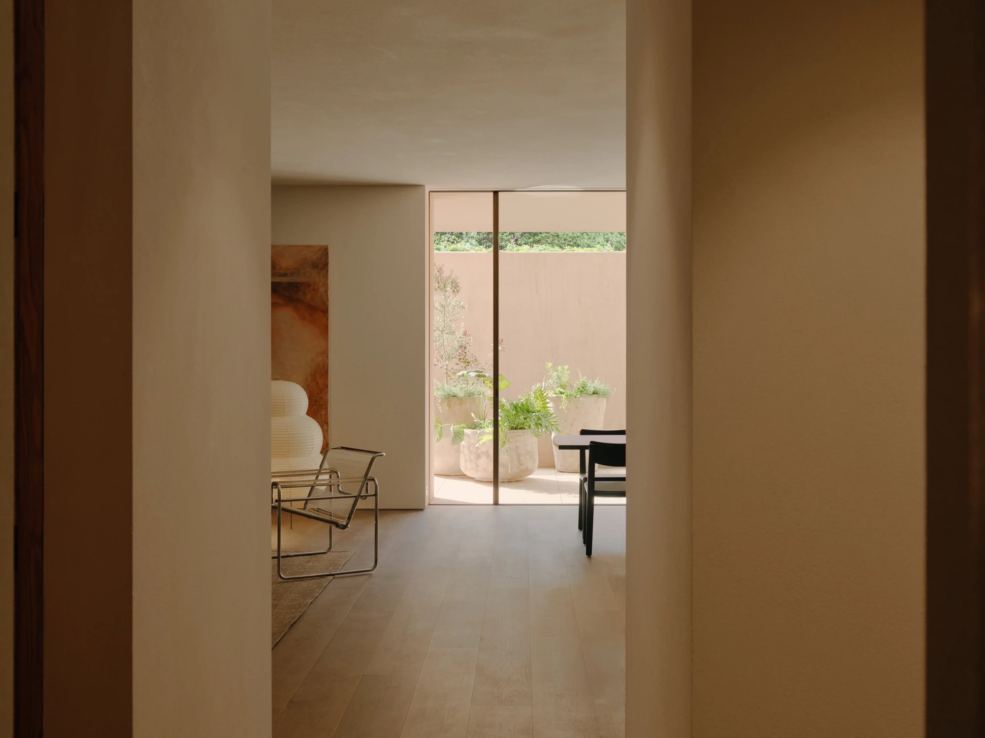 49 Walsh Street by MORQ, photographed by Tom Ross — A view down a corridor framed by earth render walls, with a tubular steel chair, a ribbed paper lamp and an earth-toned painting in the room beyond.