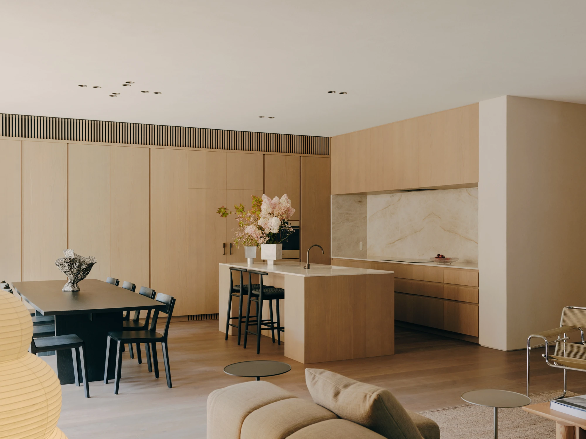 49 Walsh Street by MORQ, photographed by Tom Ross — A kitchen with a stone-topped timber island, black bar stools and a veined stone splashback, hydrangeas cut and set on the bench.