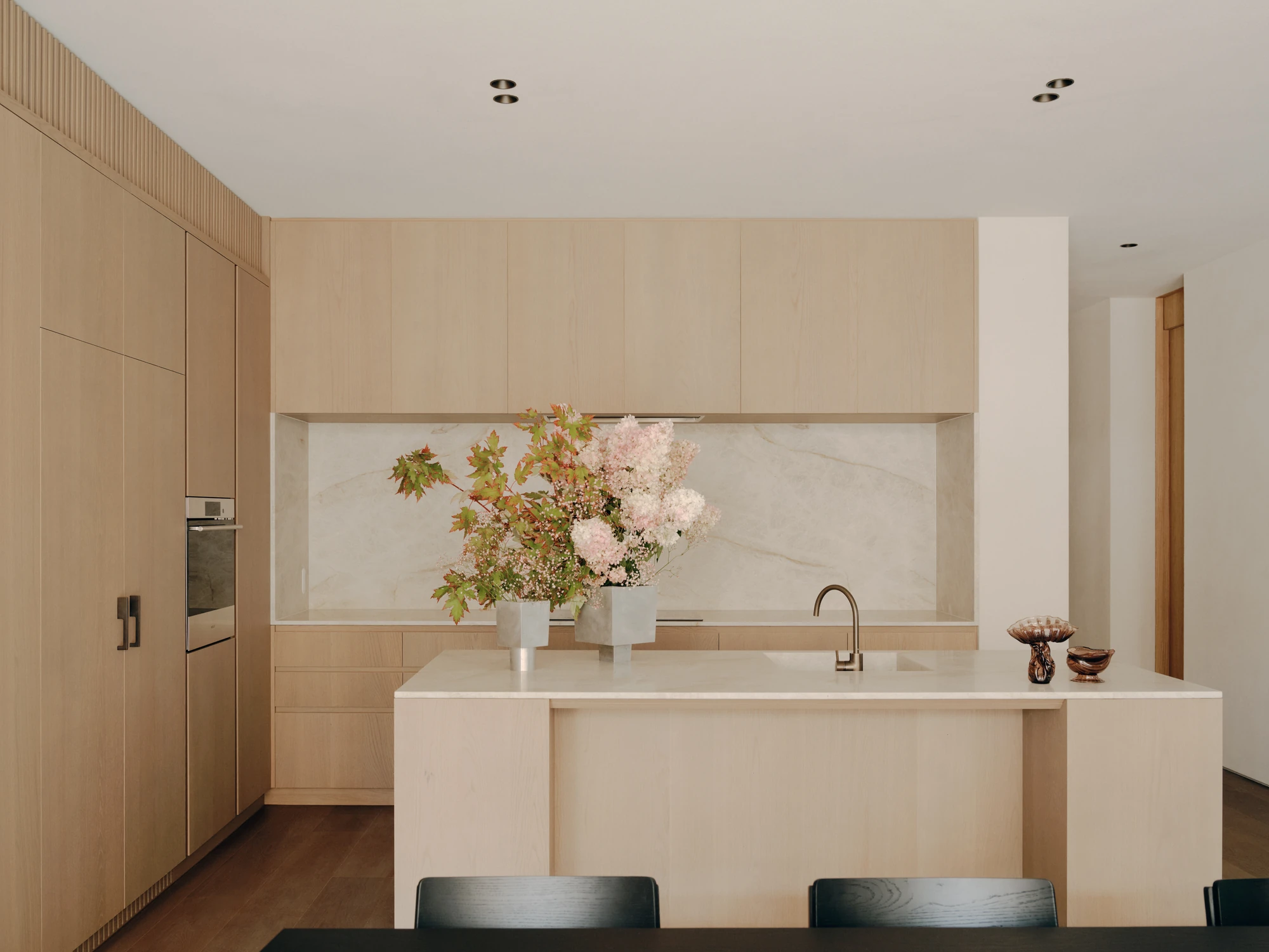 49 Walsh Street by MORQ, photographed by Tom Ross — A kitchen with pale timber cabinetry, an integrated oven and a veined stone splashback set into a recess.