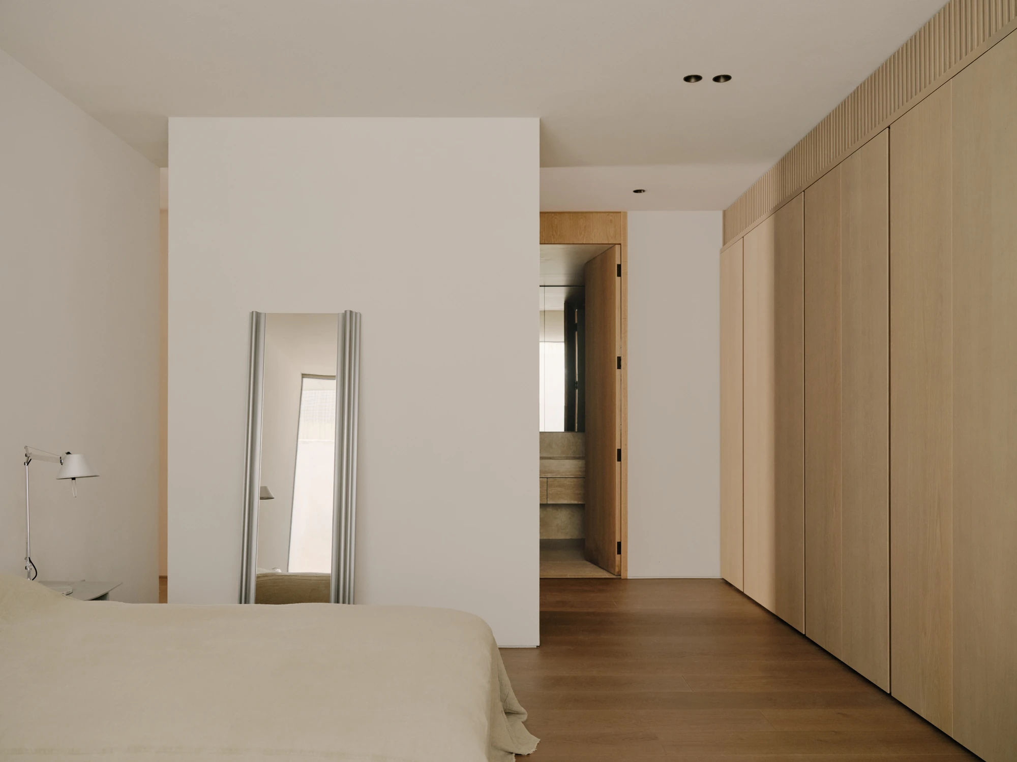 49 Walsh Street by MORQ, photographed by Tom Ross — A bedroom with a freestanding partition wall, a leaning full-length mirror and a run of pale timber wardrobes.