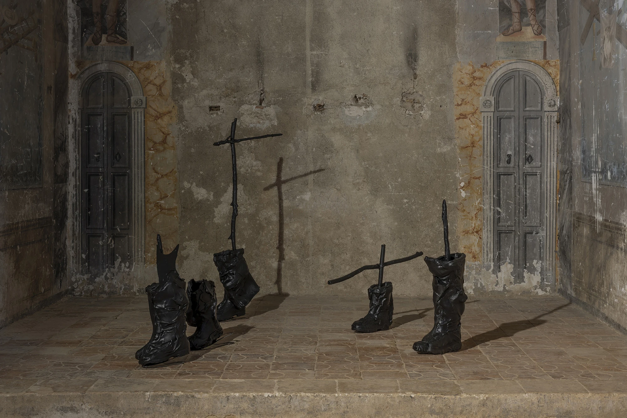KIN TOO by Spiritvessel, photographed by Roberto Ruiz — Detail of Sahatsa Jauregi's Pájaros, the blackened boots and slender steel crosses casting cross-shaped shadows against the chapel's weathered wall.