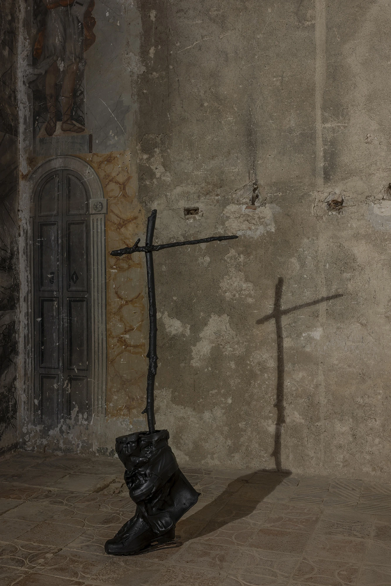 KIN TOO by Spiritvessel, photographed by Roberto Ruiz — A single boot from Sahatsa Jauregi's Pájaros, a slender cut-steel cross rising from its shaft, its shadow doubling the cross on the wall behind.