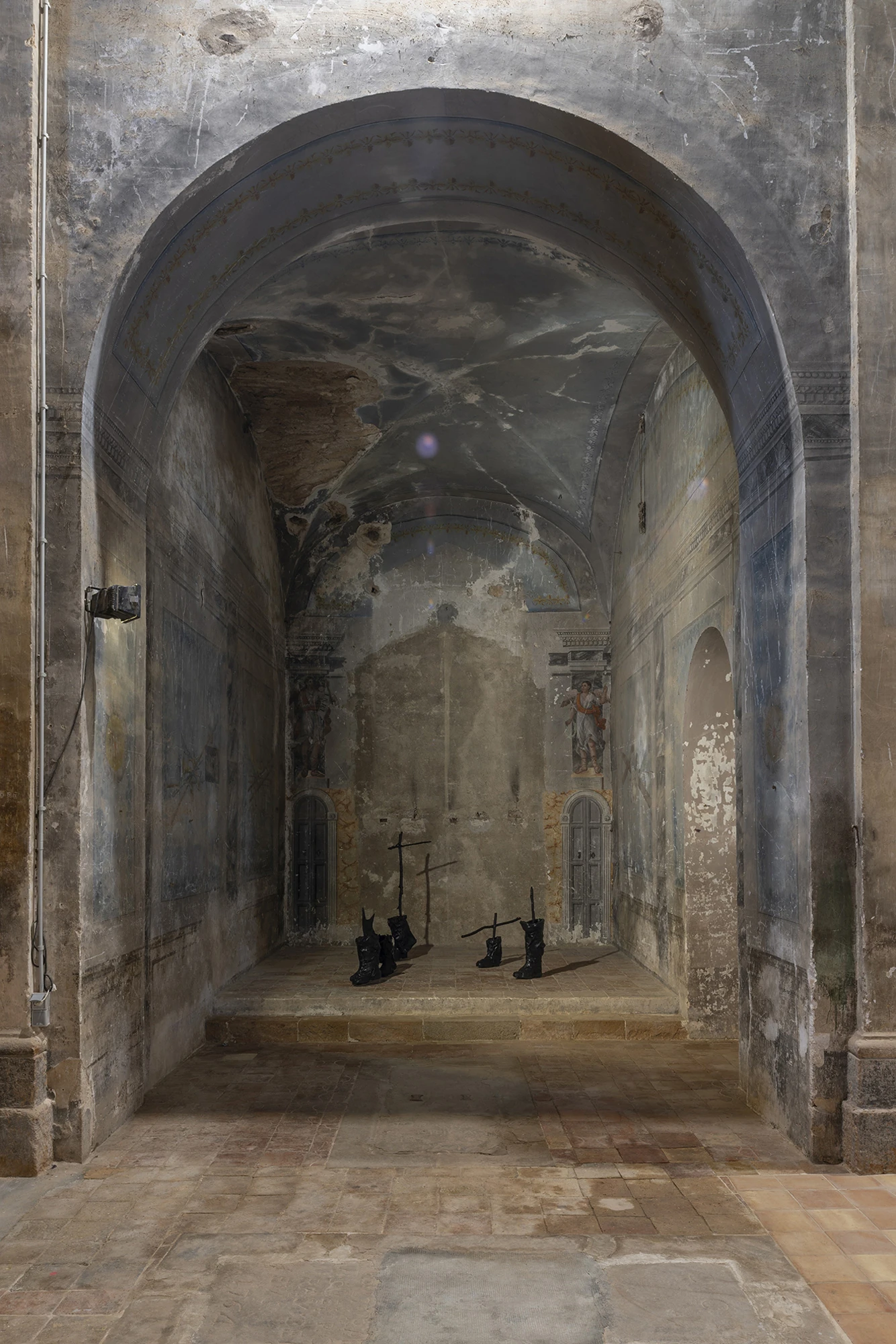 KIN TOO by Spiritvessel, photographed by Roberto Ruiz — Sahatsa Jauregi's Pájaros in a vaulted side chapel: blackened rubber-boot forms and thin cut-steel crosses arranged on a raised stone platform beneath faded frescoes.