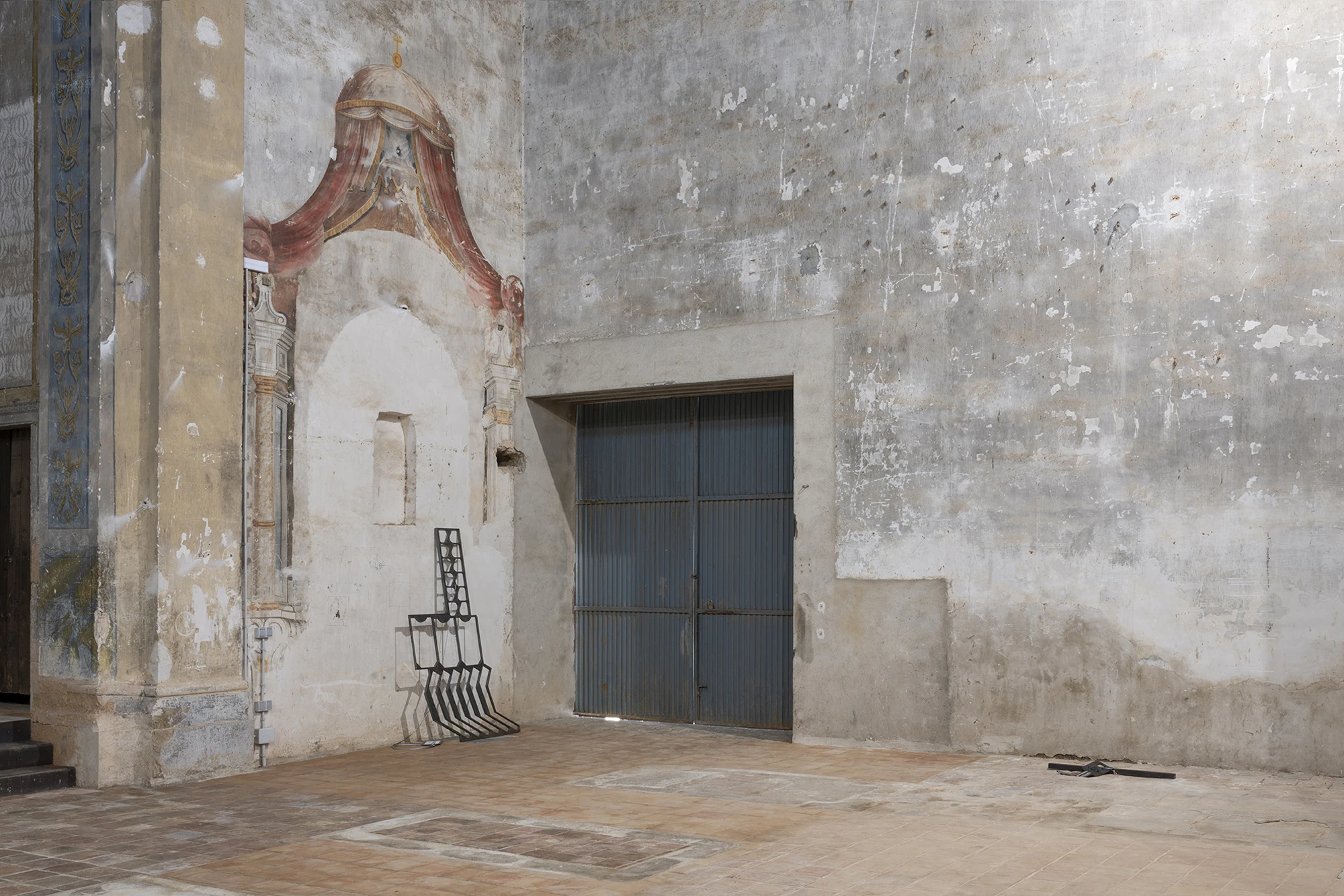 KIN TOO by Spiritvessel, photographed by Roberto Ruiz — Jordi Mitjà's steel grille leaning in a frescoed corner near a corrugated metal door, its cabled metal tag lying on the floor.