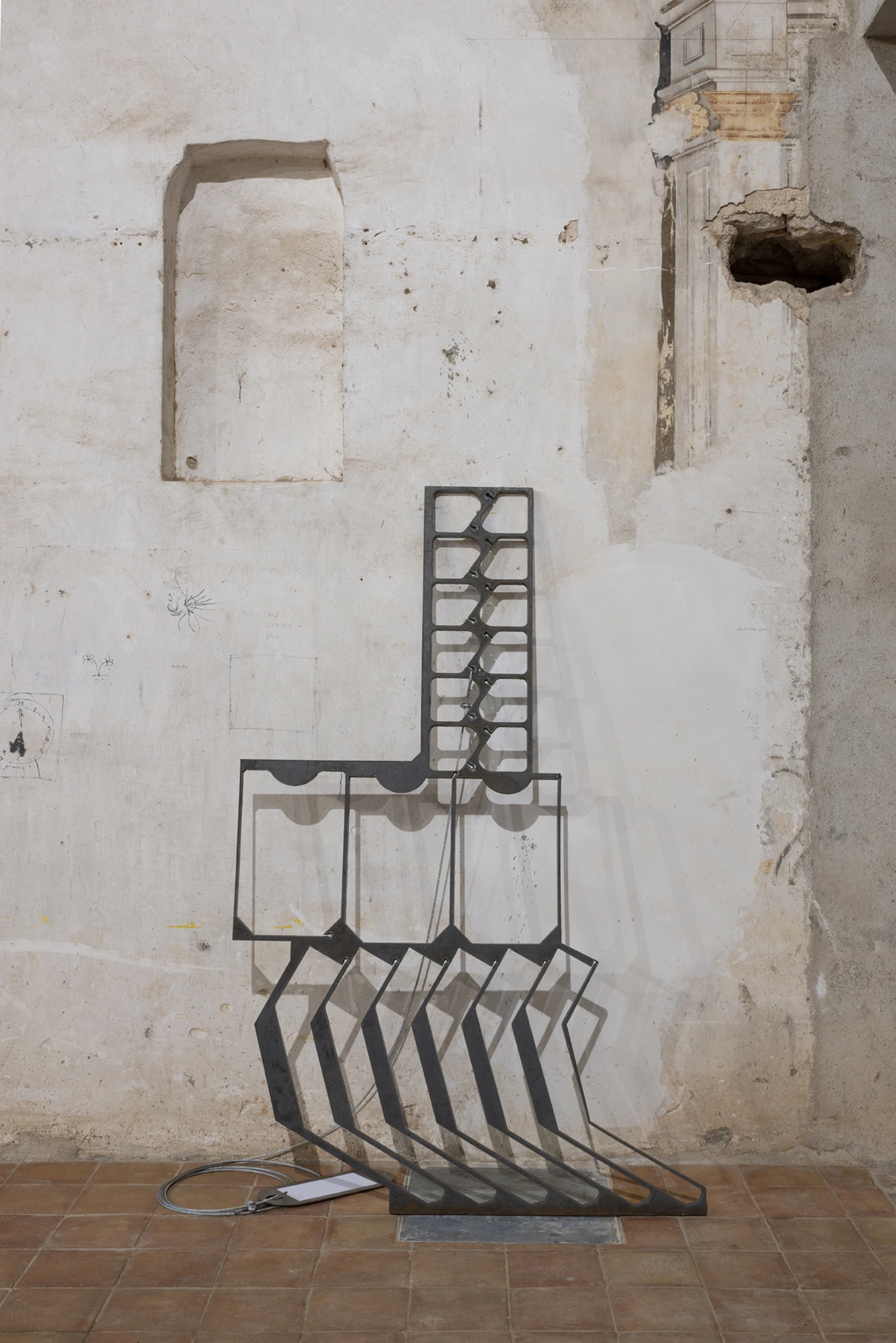 KIN TOO by Spiritvessel, photographed by Roberto Ruiz — Install view of a side wall: Jordi Mitjà's leaning steel grille and a length of iron bar set against the church's stripped plaster and a boarded doorway.
