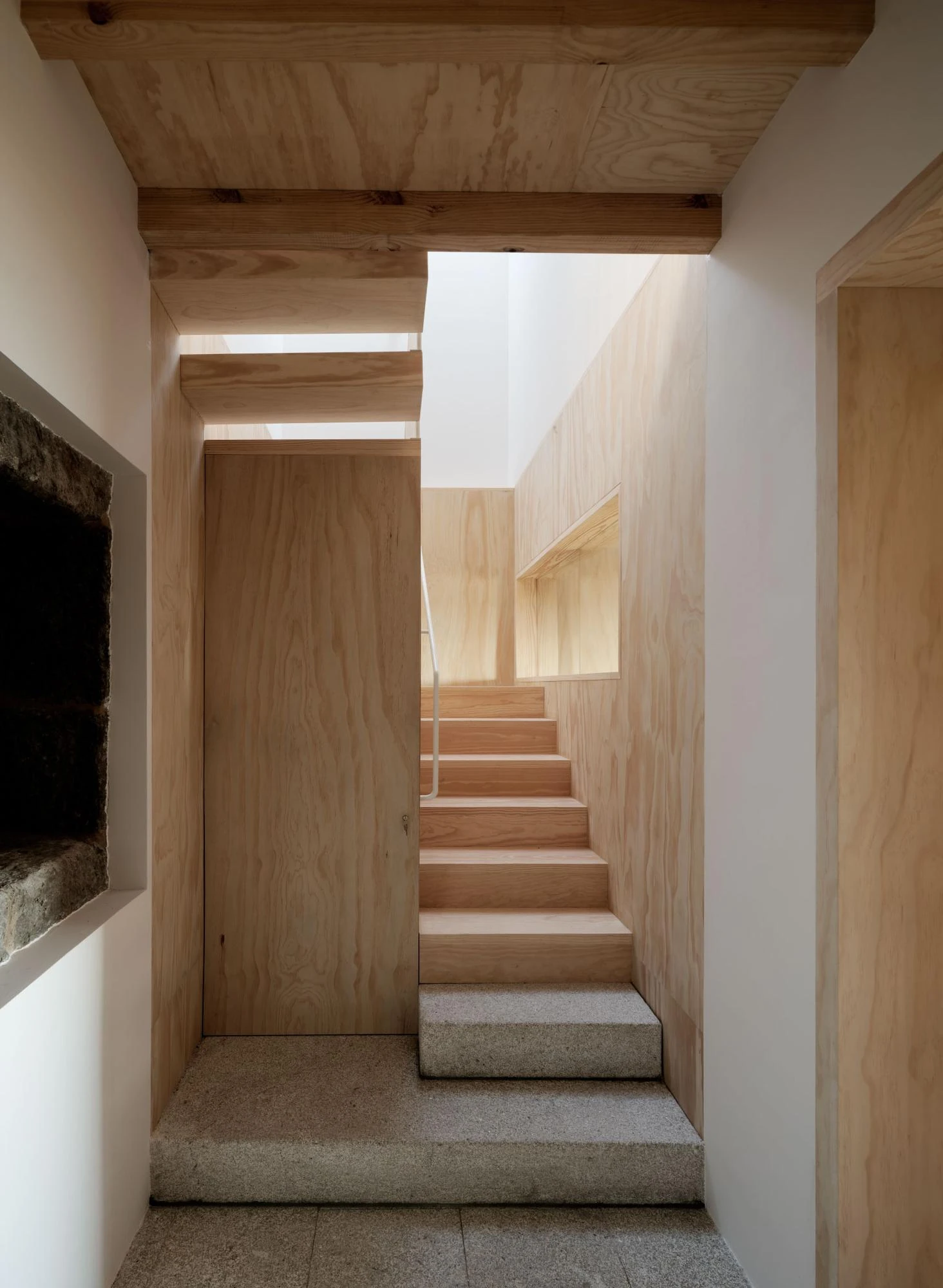 Muimenta Multipurpose Social Center by FIRM + BASED, photographed by Luis Díaz Díaz — A stair lined in pale timber turns on solid granite treads beneath a top-lit landing.