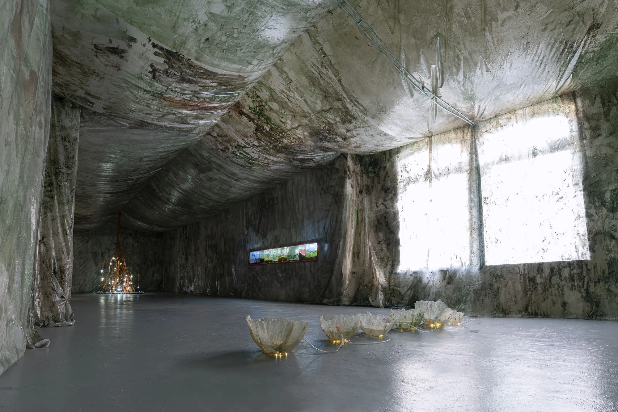 Paulina Mellado at MAC, Santiago by MAC Santiago — Wide view of the exhibition, the museum interior wrapped into a cave with sculptural elements set across the floor and daylight entering at the far wall.