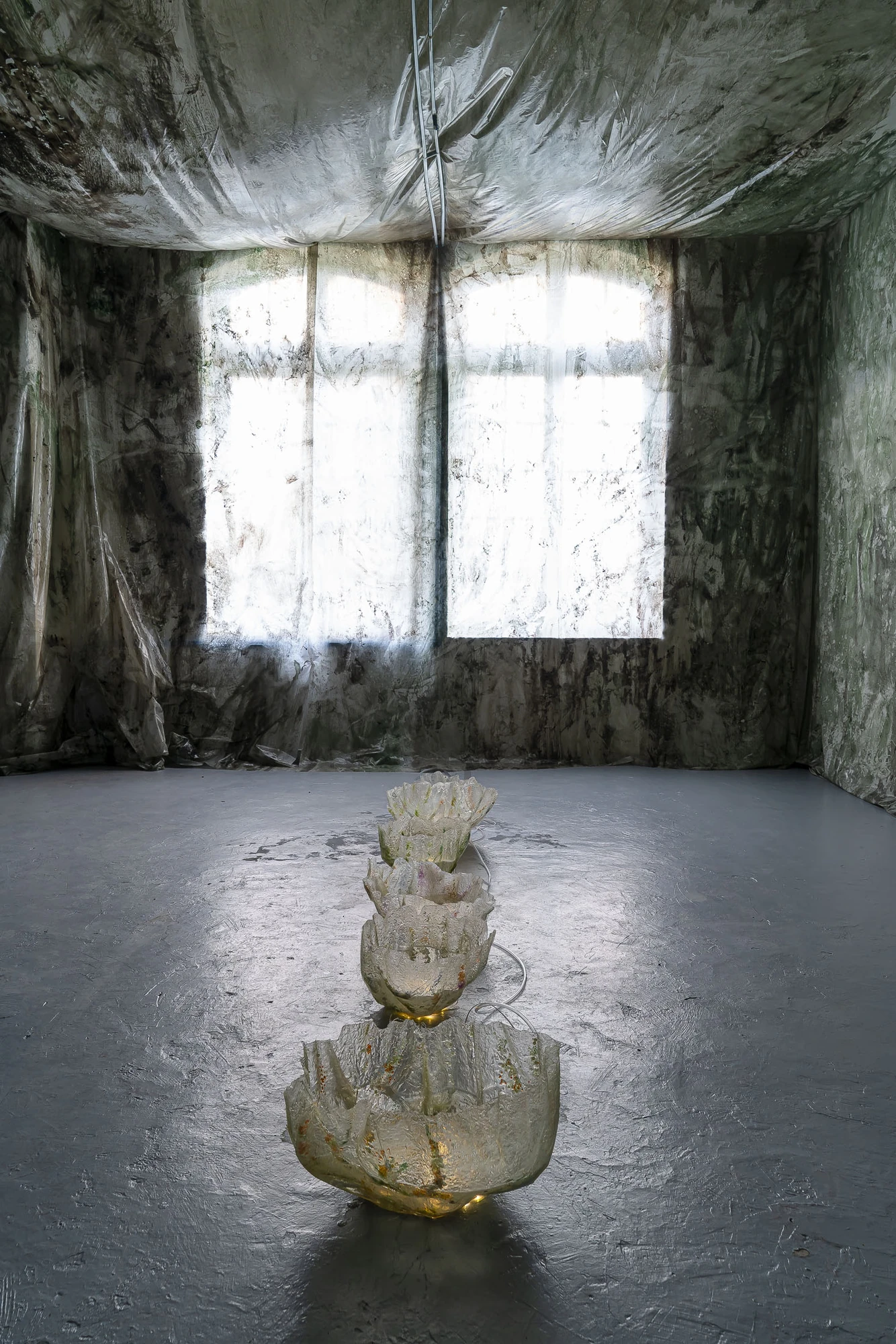 Paulina Mellado at MAC, Santiago by MAC Santiago — A row of vessel-like sculptures runs across the floor toward the light of the far wall.