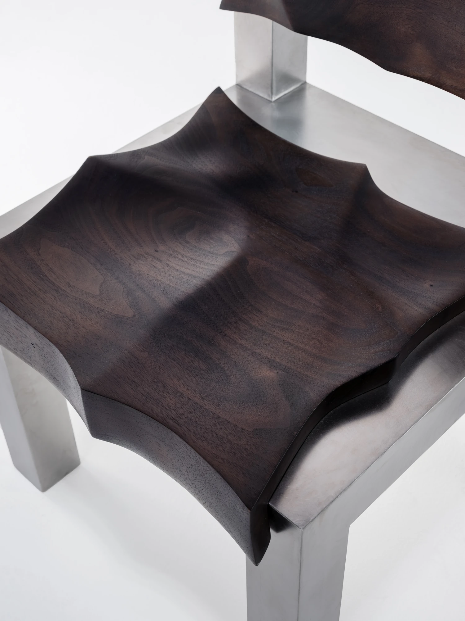 Soft Tensions by Studio Sija, photographed by Pēteris Vīksna — An overhead close view of the walnut seat, its surface carved into a soft rippling hollow that catches raking light across the grain.