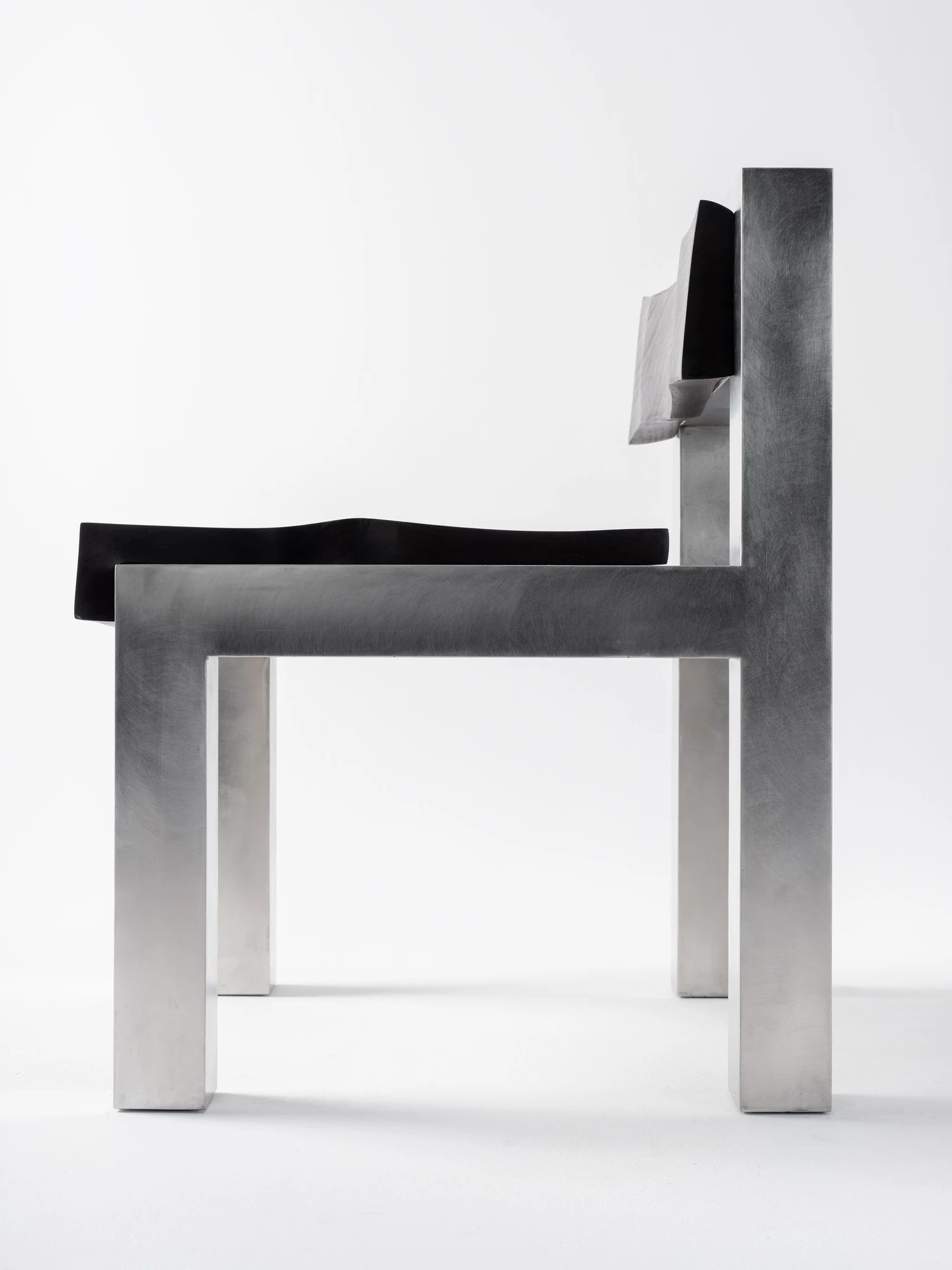Soft Tensions by Studio Sija, photographed by Pēteris Vīksna — A side elevation reducing the chair to crisp lines of welded stainless steel, the thin walnut seat floating between the square legs.